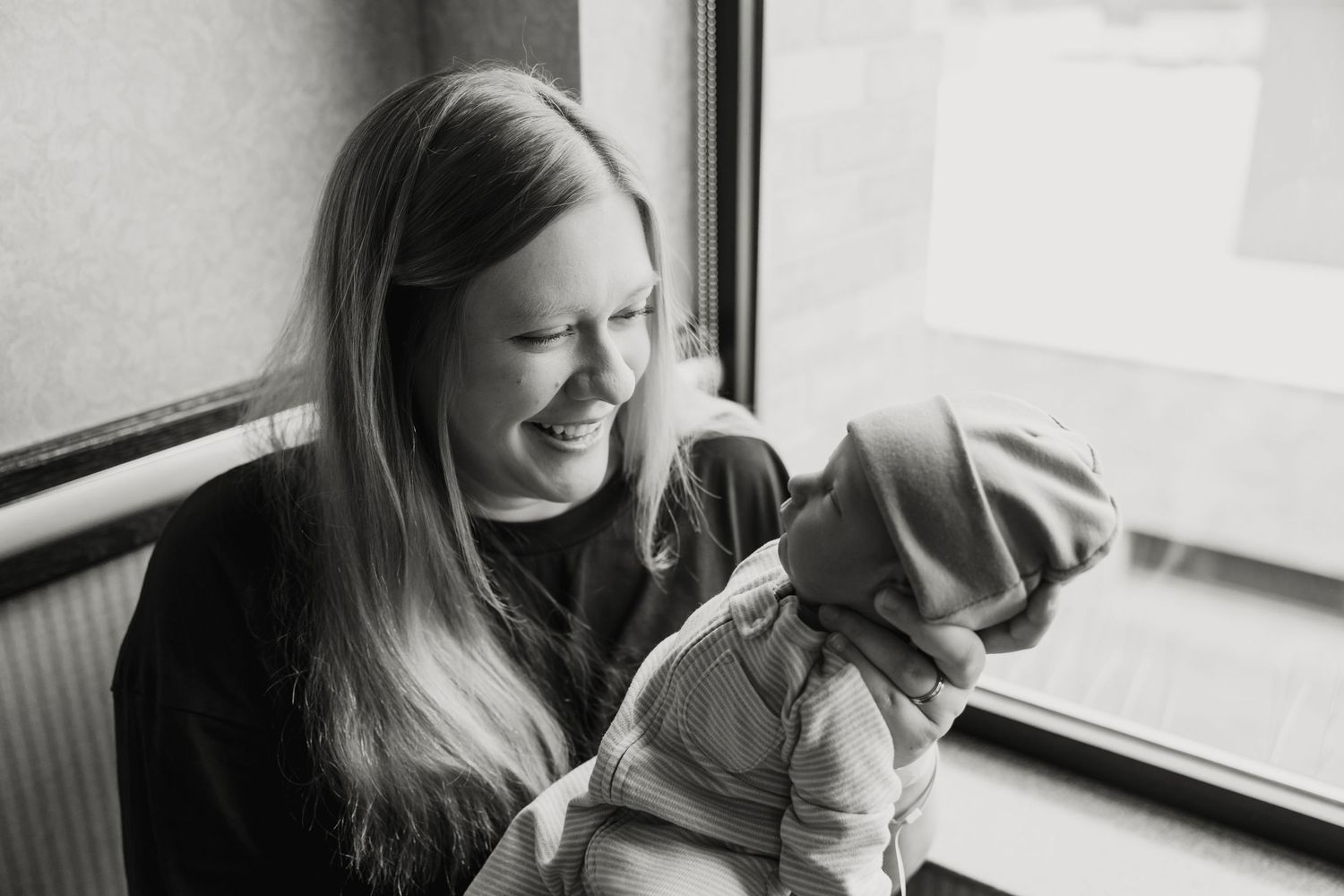 A heartwarming monochrome photo showing a mother and newborn sharing an intimate bonding moment by a window.