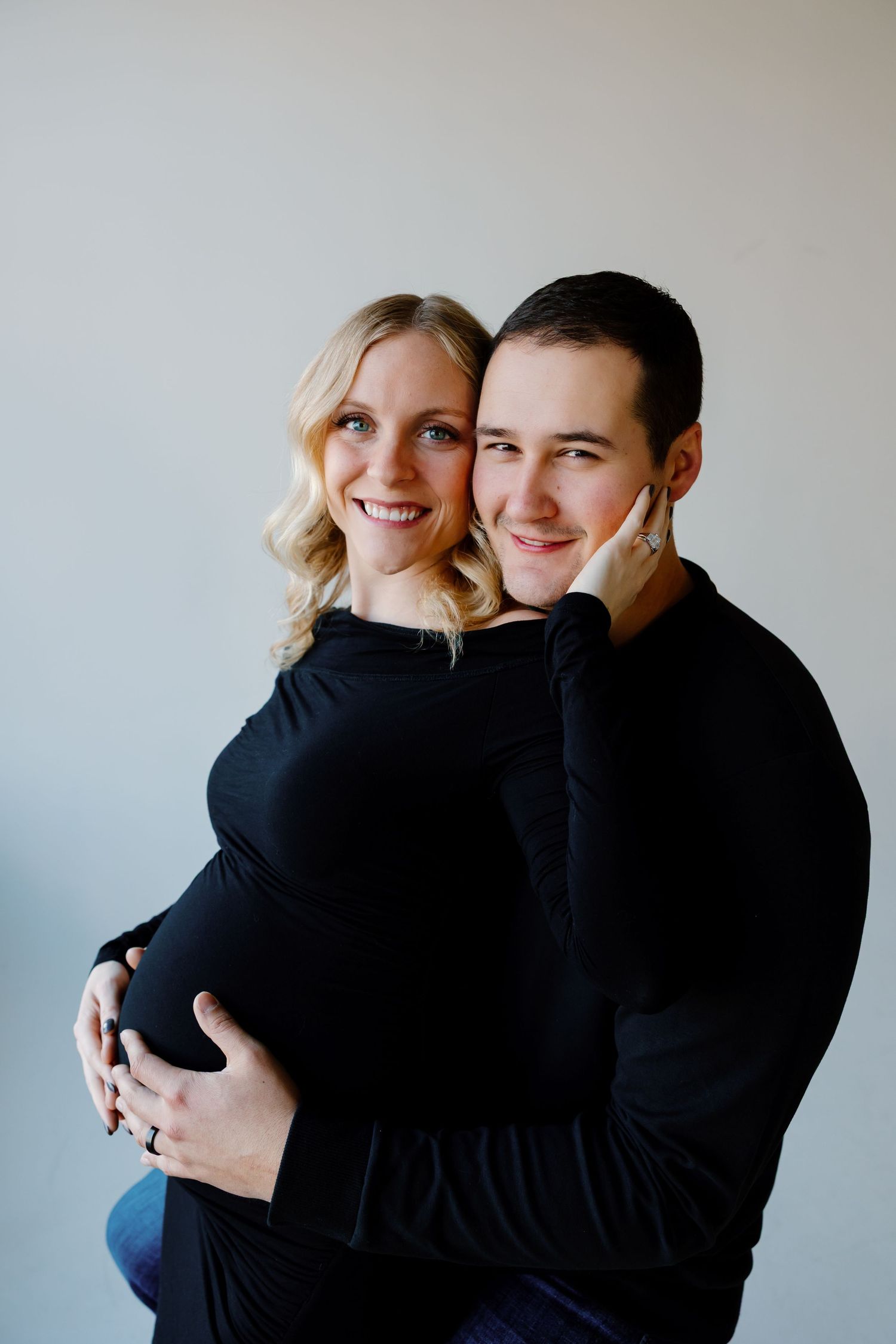 A tender maternity portrait showing a couple in black sweaters against a light background. Riley Ro Photo Sioux Falls, SD