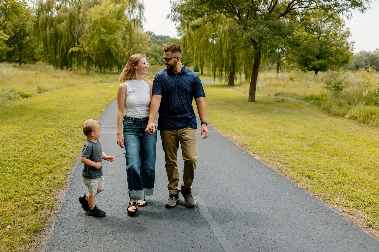 A family walks together on a tree-lined pathway enjoying a sunny day in the park.