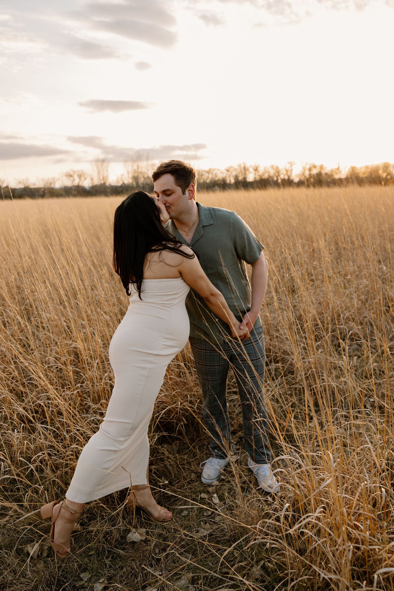 A tender moment between a couple in a sun-drenched field of tall grass at dusk.