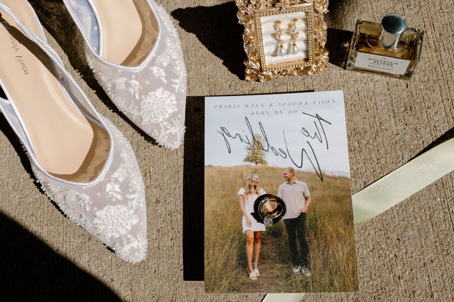 Bridal flat shoes with lace detail beside wedding program, pearl earrings, and perfume bottle on neutral background.