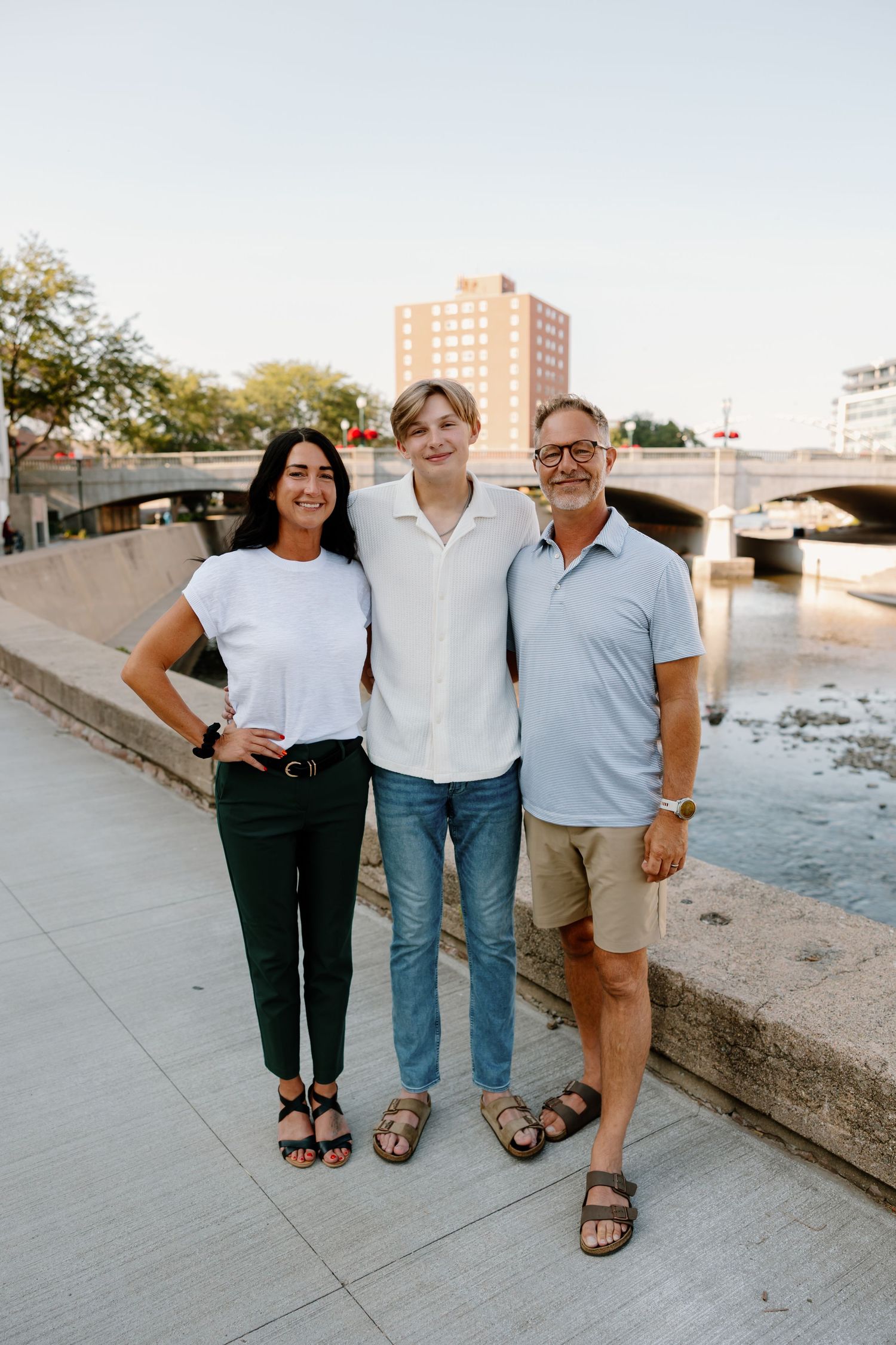 Group of three people posing casually by a waterfront on a sunny day.