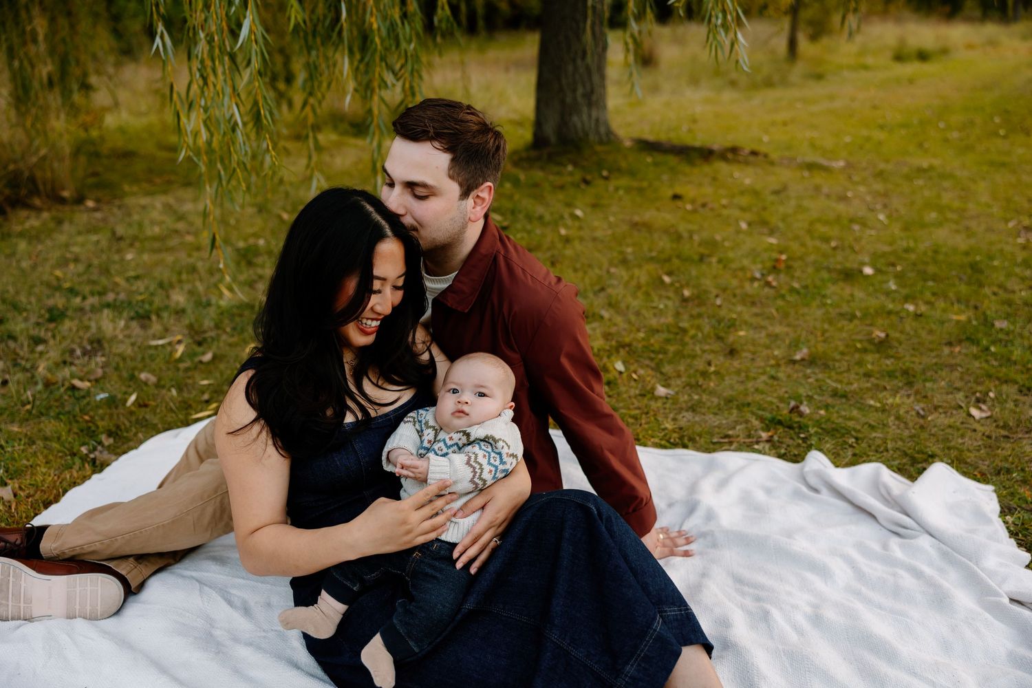 Family enjoying tender moments together outdoors on a warm autumn day in a park setting. Riley Ro Photo Sioux Falls, SD