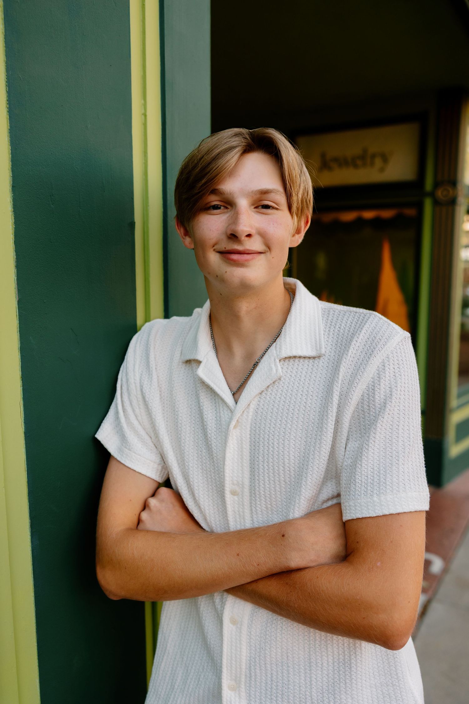 Four candid portraits of someone in a white collared shirt leaning against a storefront with natural lighting.