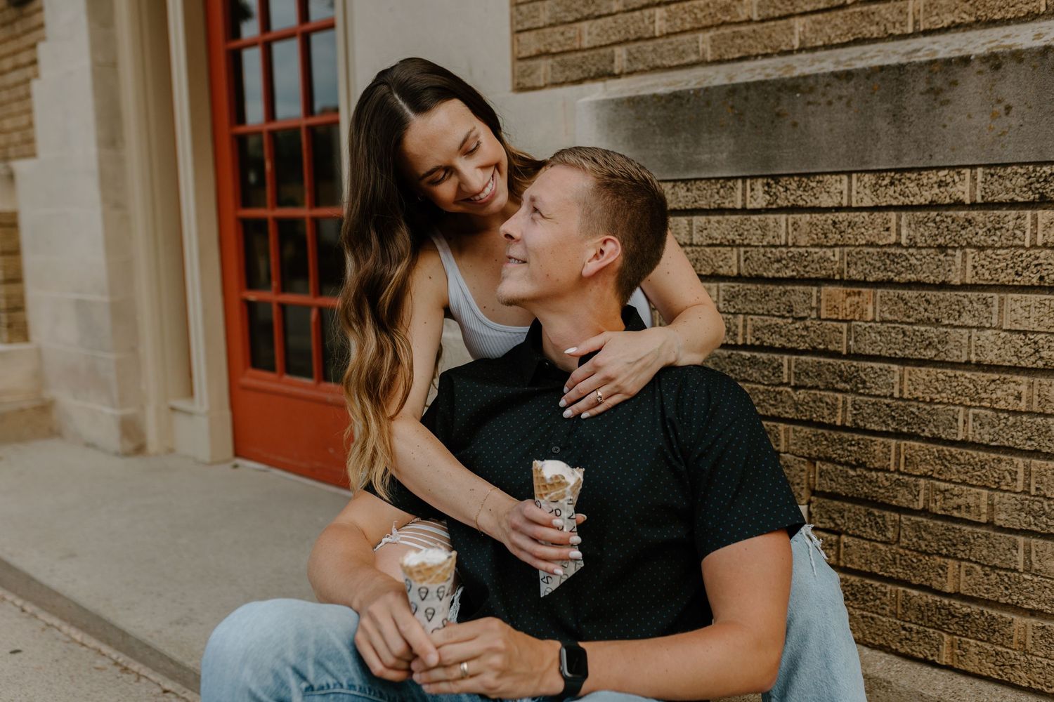 A couple sharing an intimate moment while holding drinks against a brick wall.