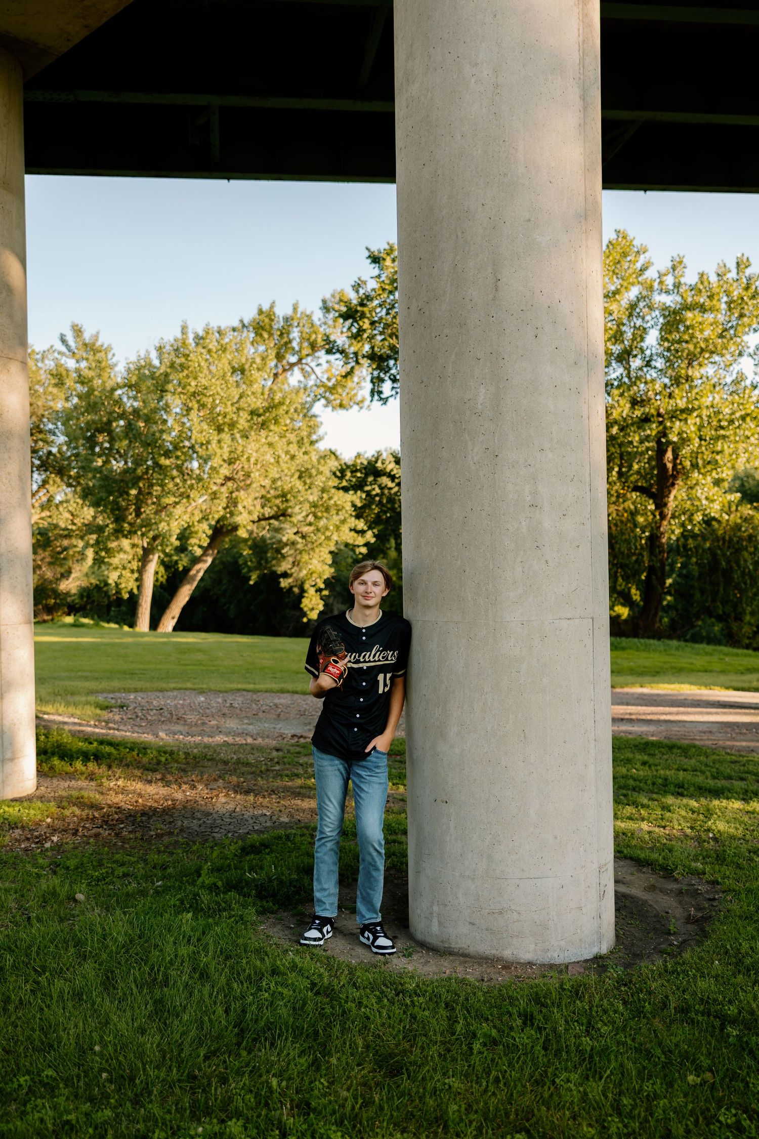 Teen athlete poses between concrete support columns at sunset in a park setting.
