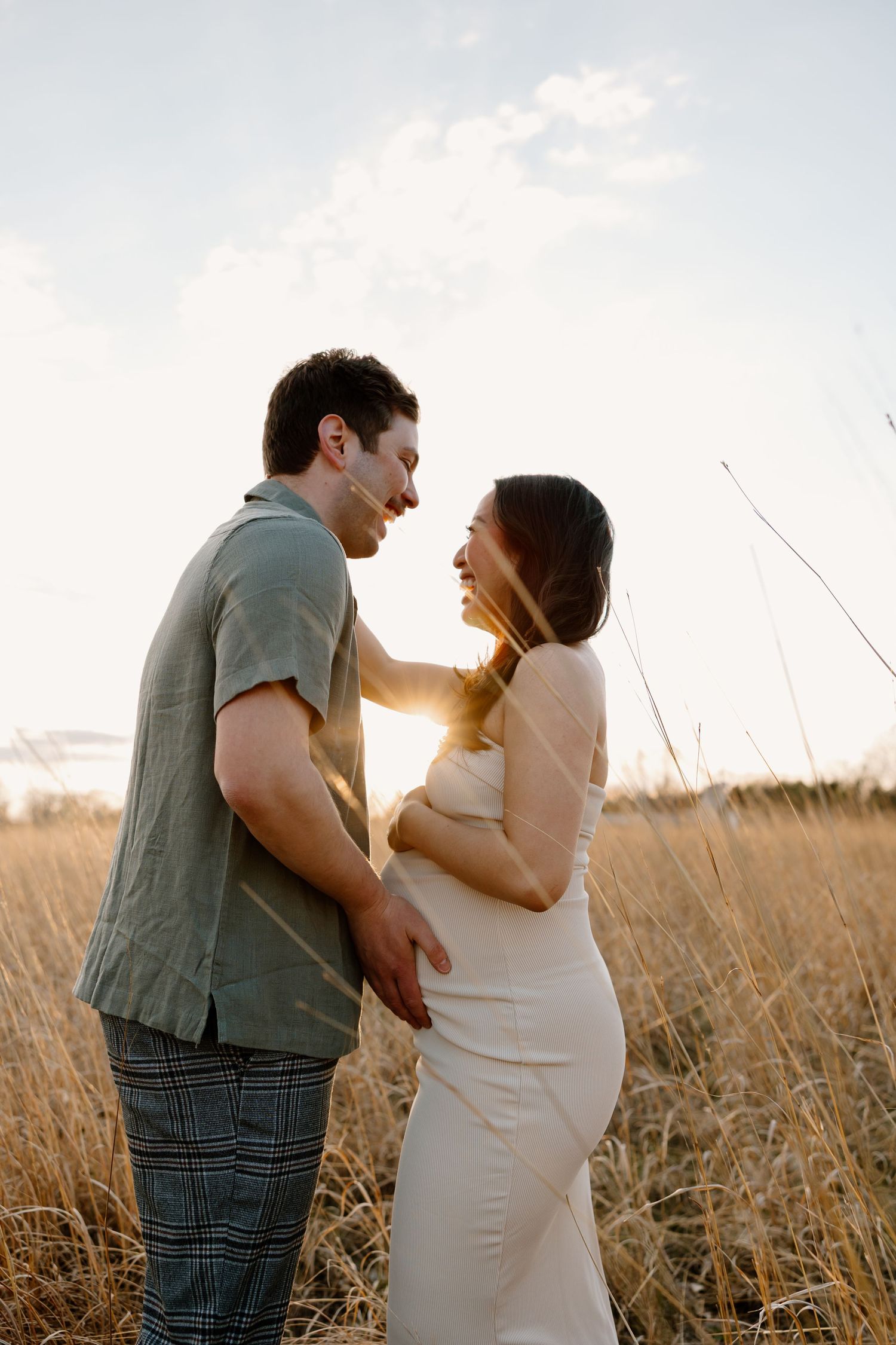 A couple shares a tender embrace in a sunlit field of wheat at sunset.