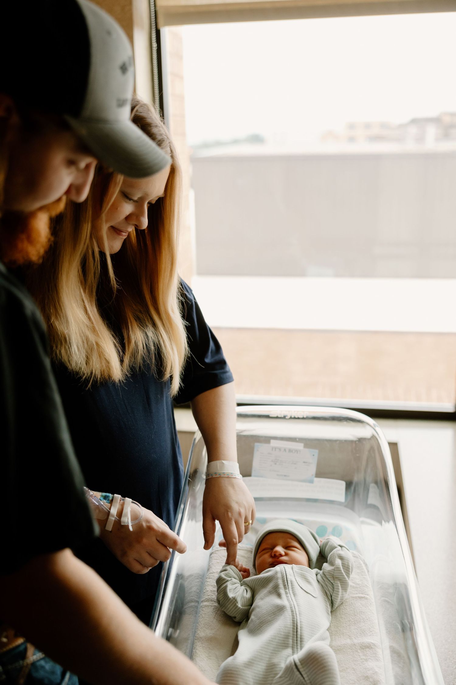 Gentle hands tend to a newborn baby resting in a hospital bassinet.