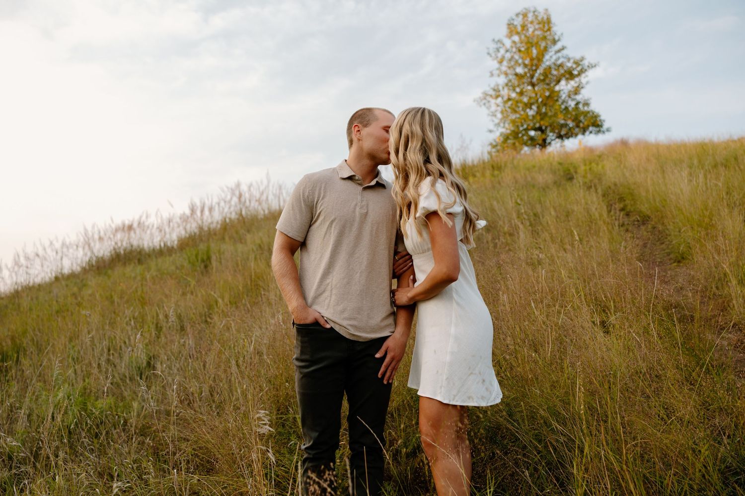 A romantic moment between a couple on a hillside with tall grass and autumn light.
