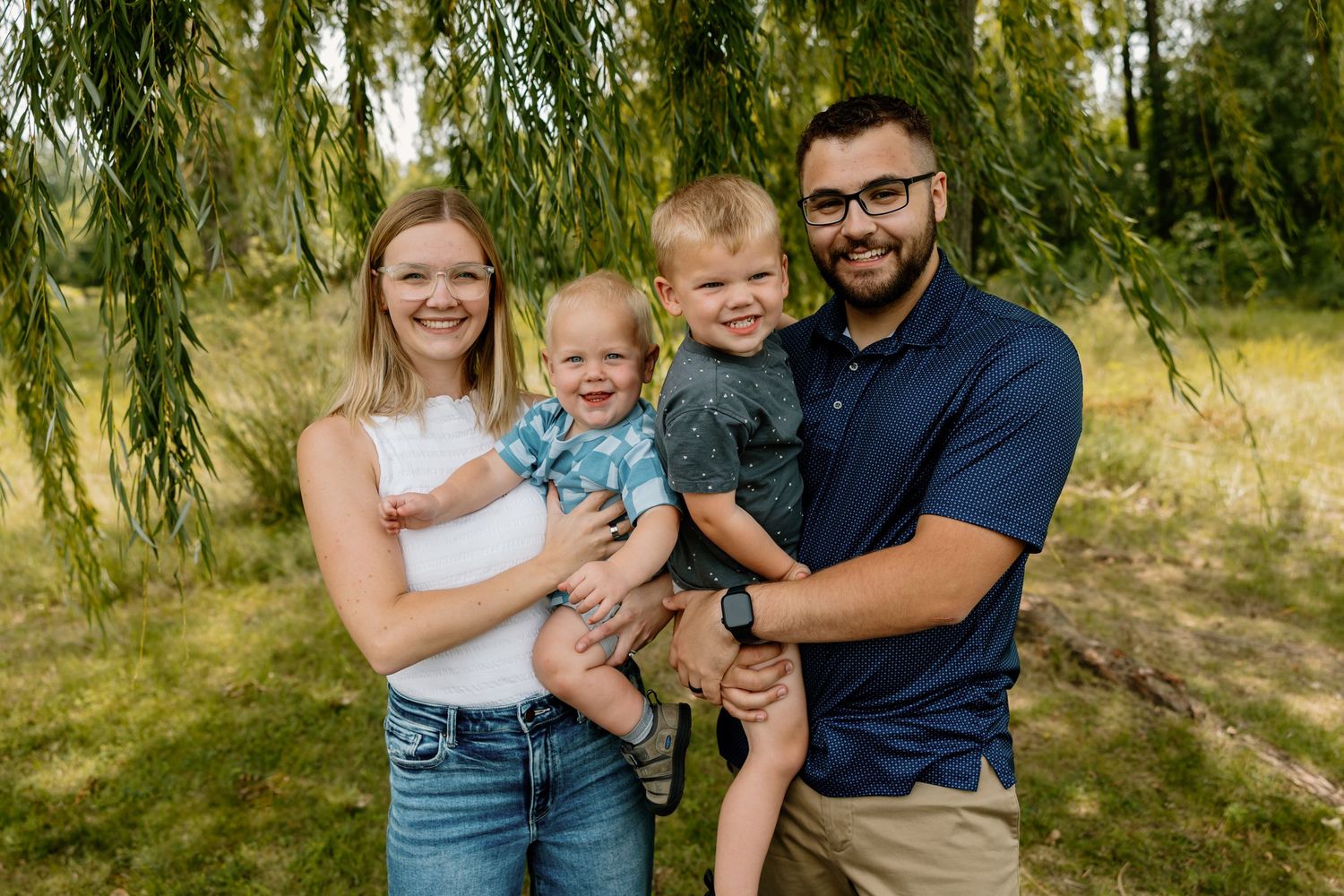 A happy looking family relaxes together under weeping willow trees on a sunny summer day.