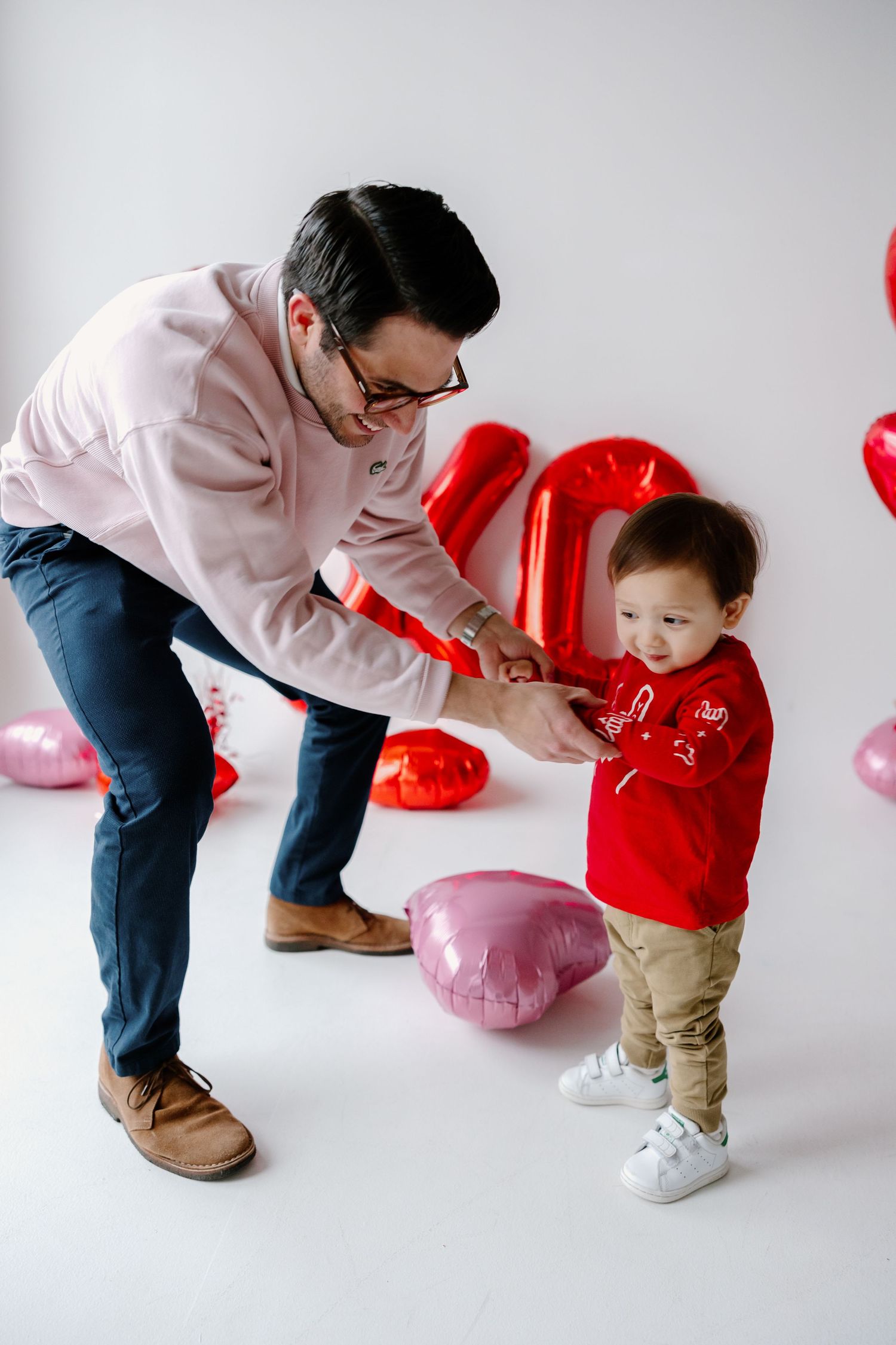 Parent and toddler enjoying playful moment with heart balloons in Valentine's Day themed photoshoot.