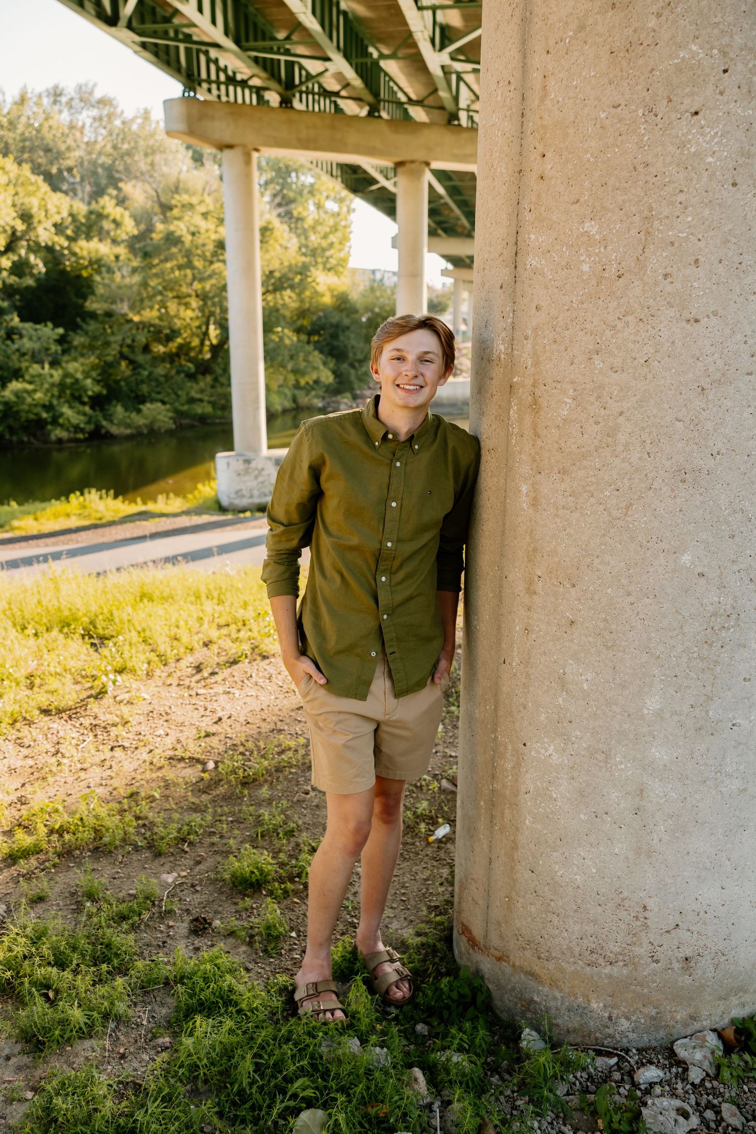 Person in olive shirt and khaki shorts stands between concrete pillars in natural setting.
