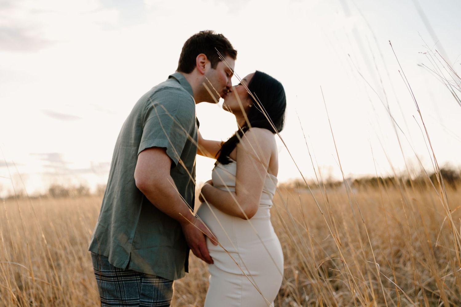 A romantic couple embraces in a sun-lit field of tall golden grass during sunset.