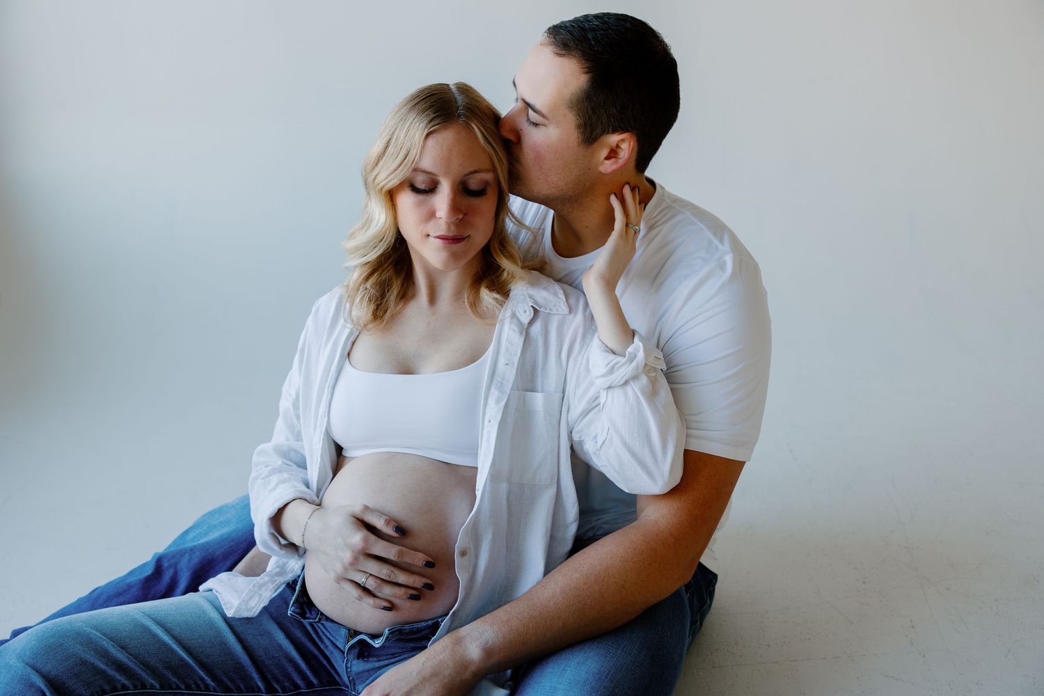 A couple in white clothing sits together intimately on a couch during a lifestyle photography session. Riley Ro Photo Sioux Falls, SD