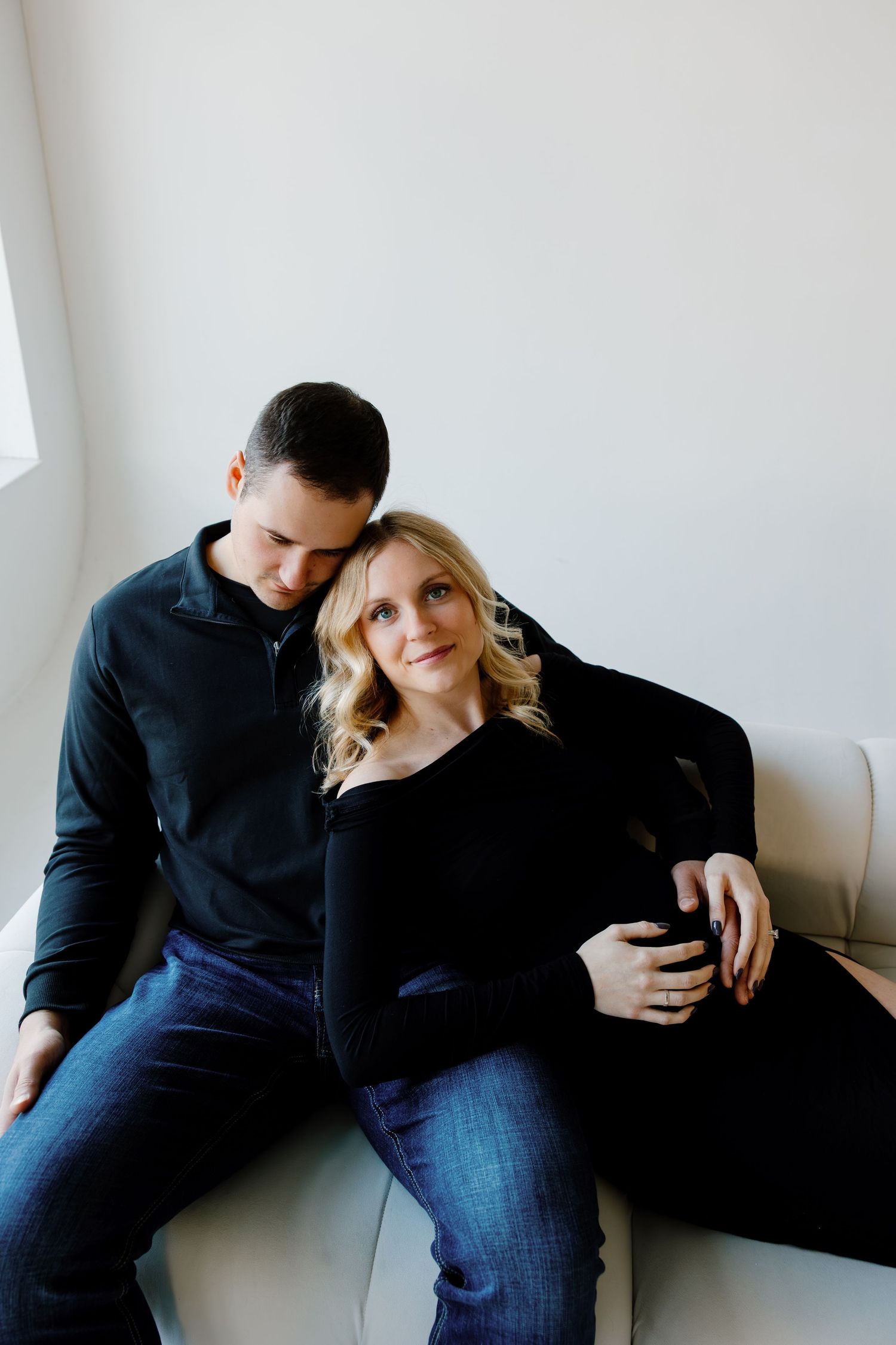 A couple in dark clothing reclines against a white wall in a series of intimate poses. Riley Ro Photo Sioux Falls, SD
