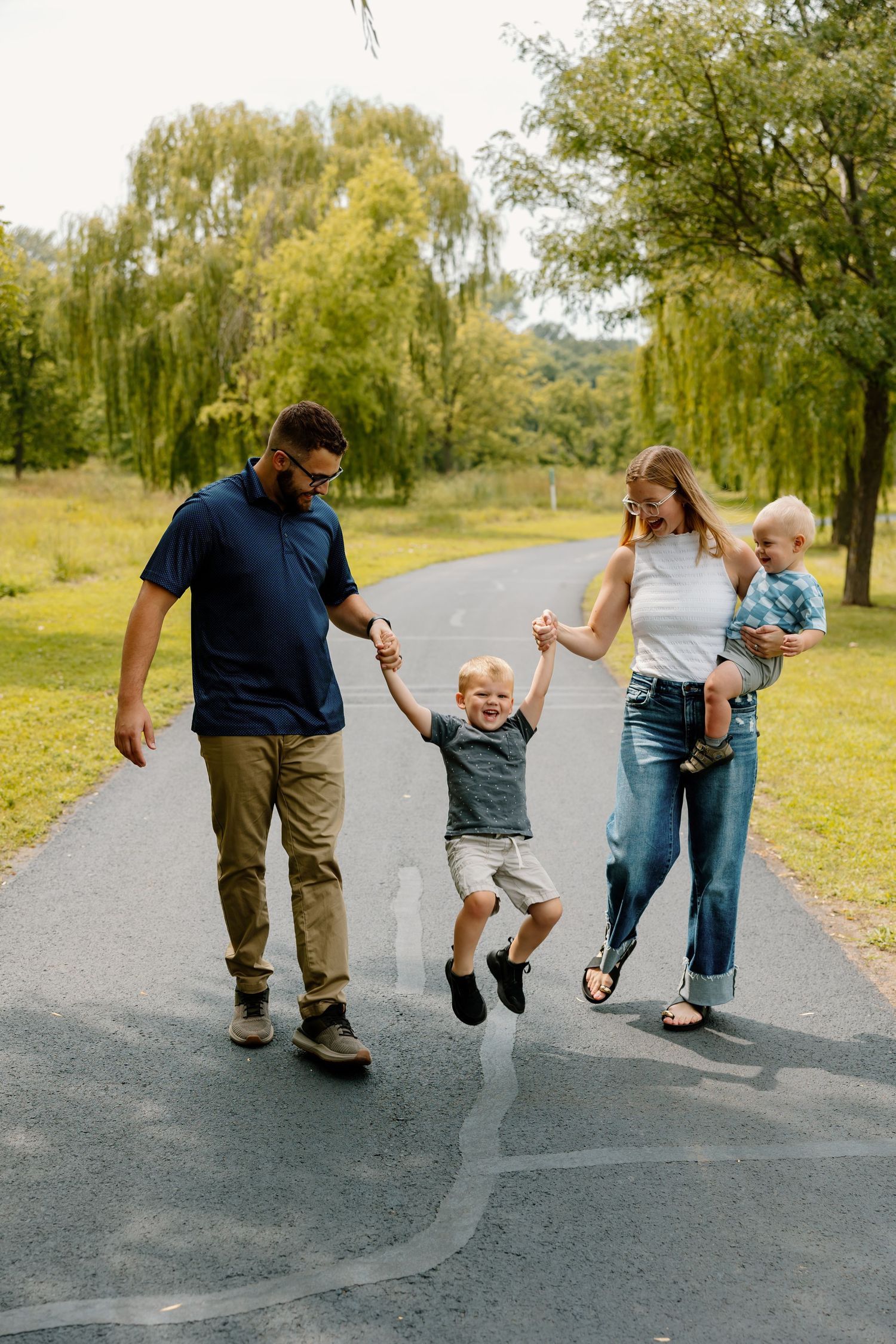 Family enjoys active moment together on paved path under weeping willow trees.