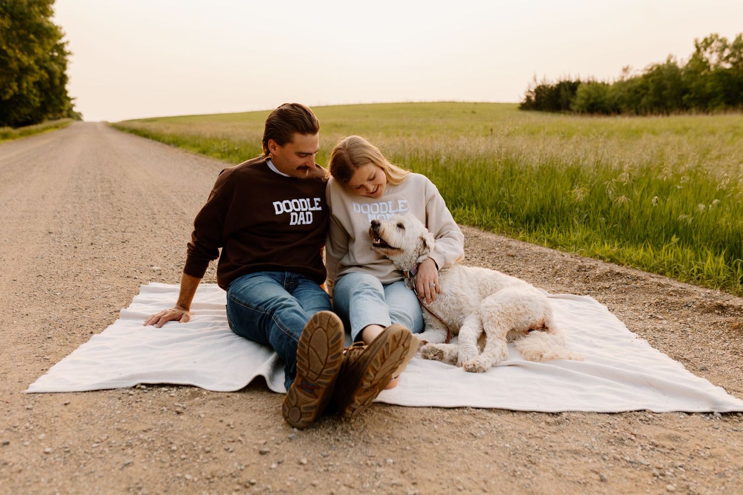 Couple relaxes on blanket with dog on rural dirt road surrounded by green fields.
Sioux Falls Photographer  
Evermore Photo Co