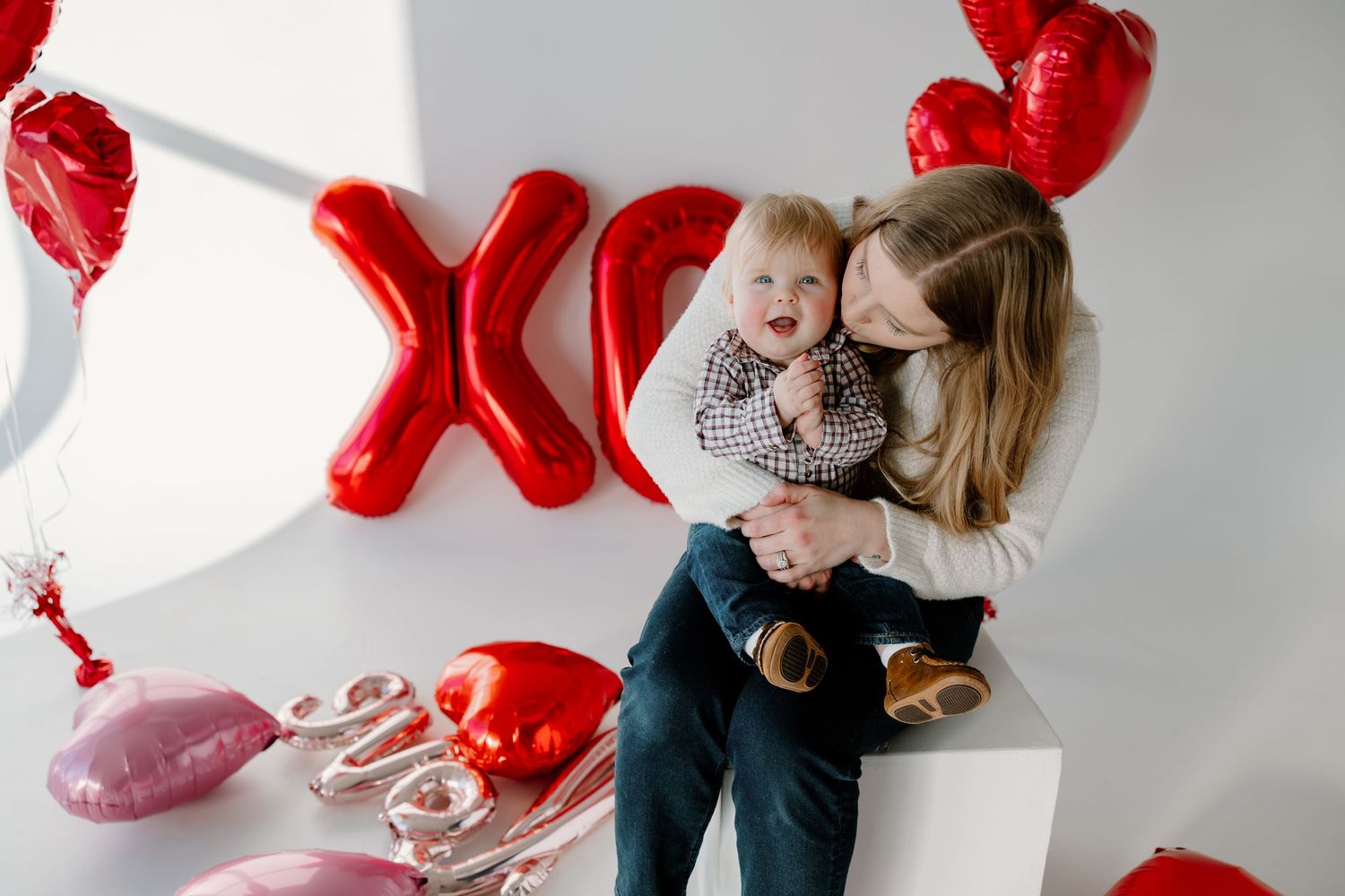 Valentine's scene with red XOXO balloons, heart decorations and balloon garland in white studio setup.