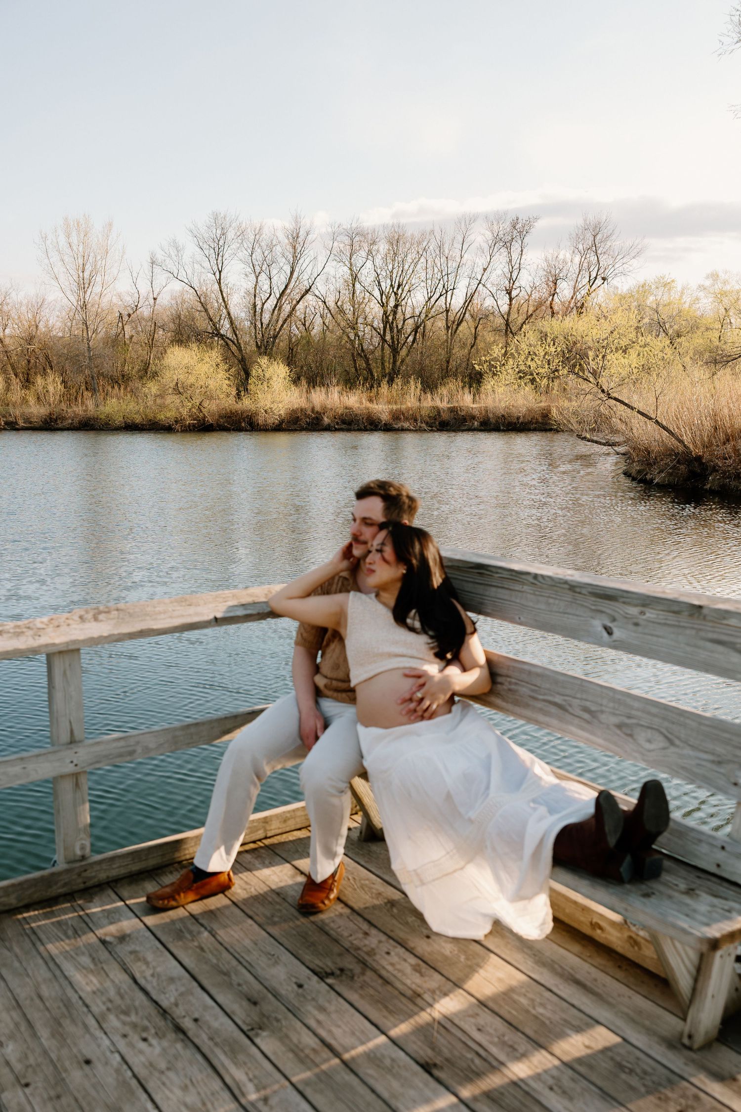 A couple relaxes on a wooden dock overlooking a tranquil lake during sunset in autumn.