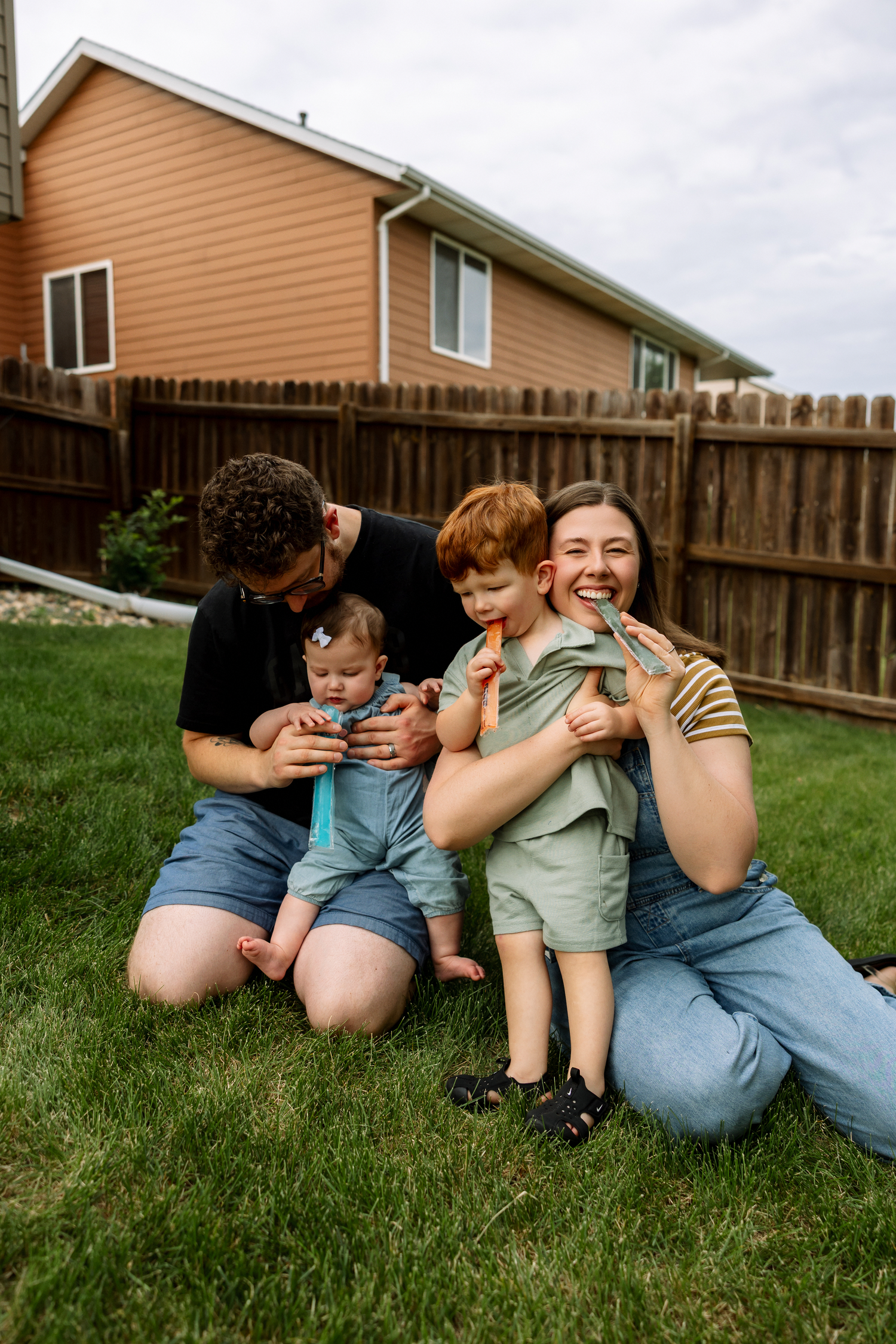 Joyful family of four laughing together on green grass in suburban backyard.