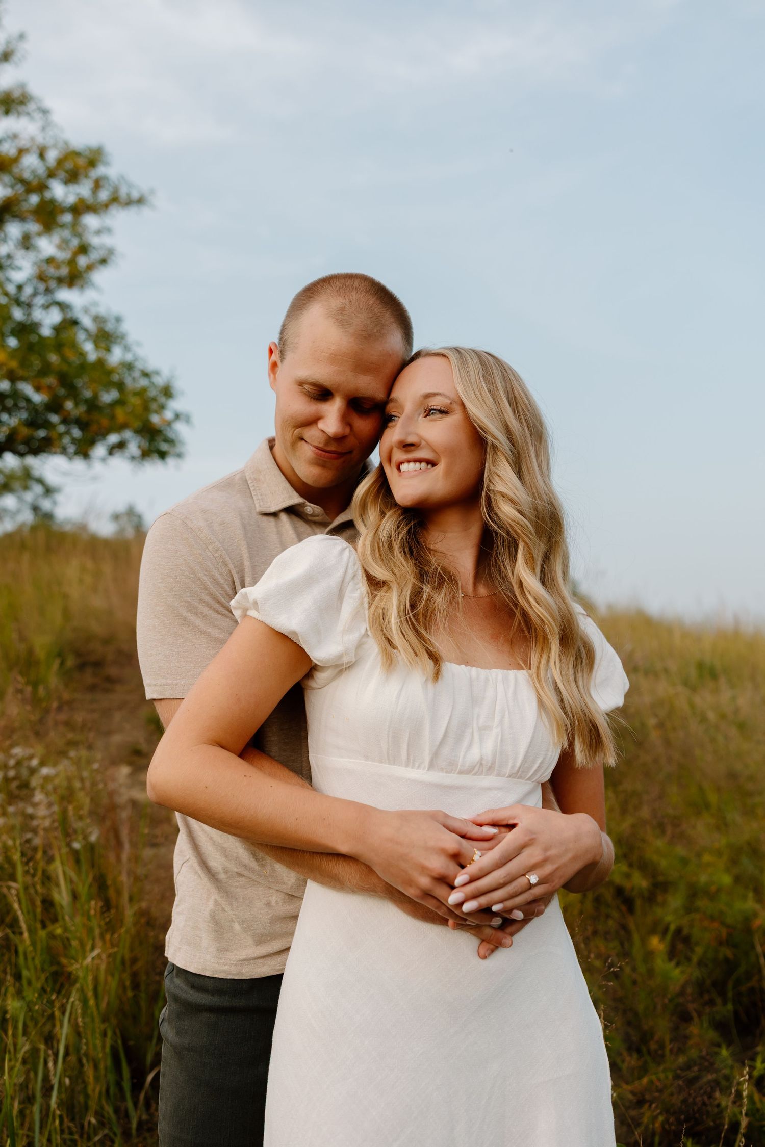 A couple laughs together while embracing in a scenic outdoor setting with golden light.