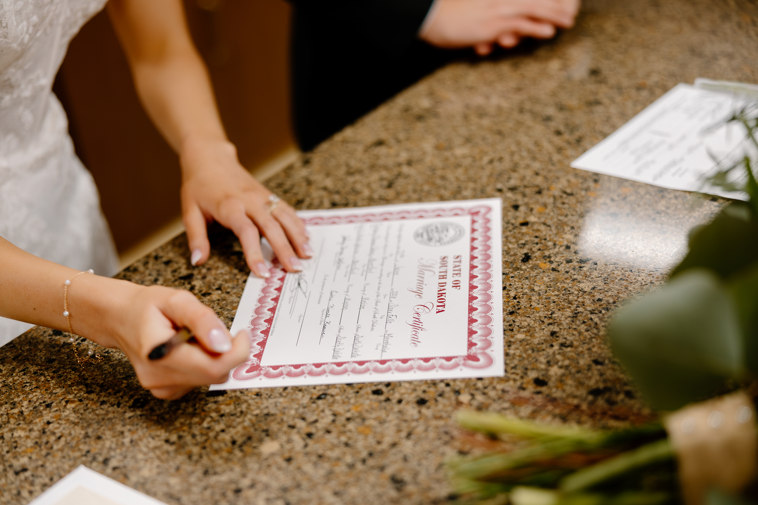 Bride signing wedding marriage certificate at granite counter with pen during wedding ceremony.