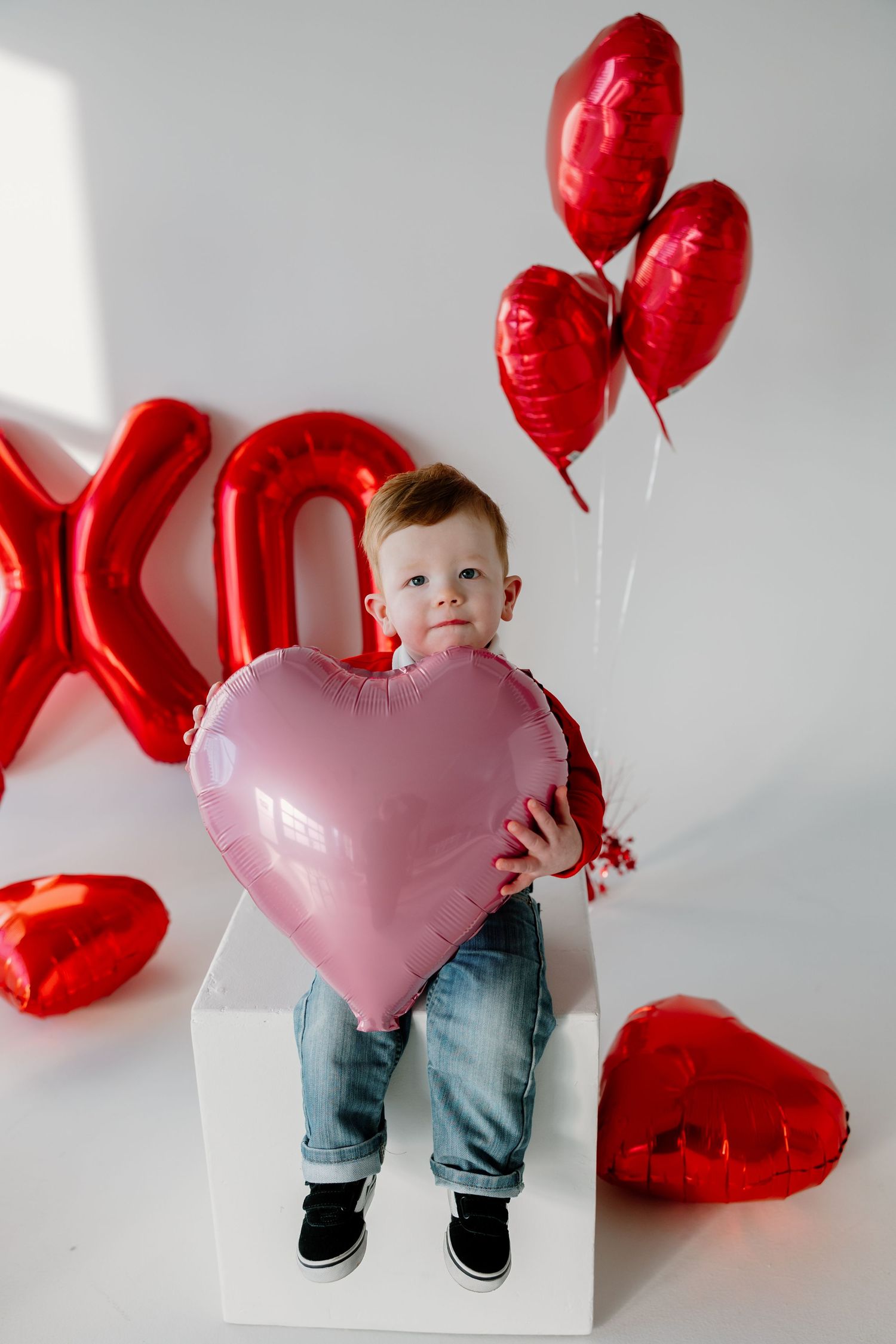 Valentine's Day themed photo setup with red and pink heart balloons against white background.