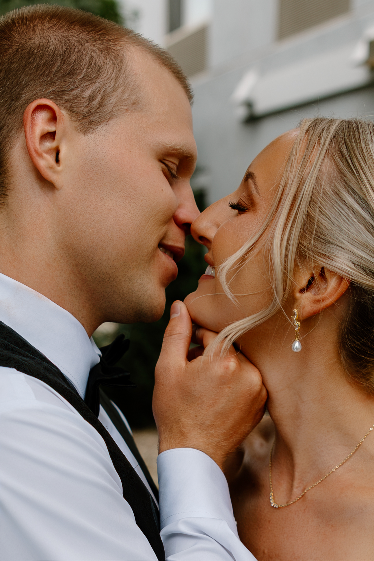 A bride and groom share a romantic almost-kiss moment, with the groom in a black bow tie and bride wearing pearl drop earrings.