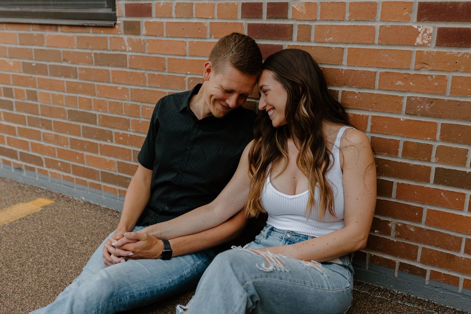 A couple sitting together and laughing against a brick wall background wearing casual denim outfits.
Sioux Falls Photographer  
Evermore Pho