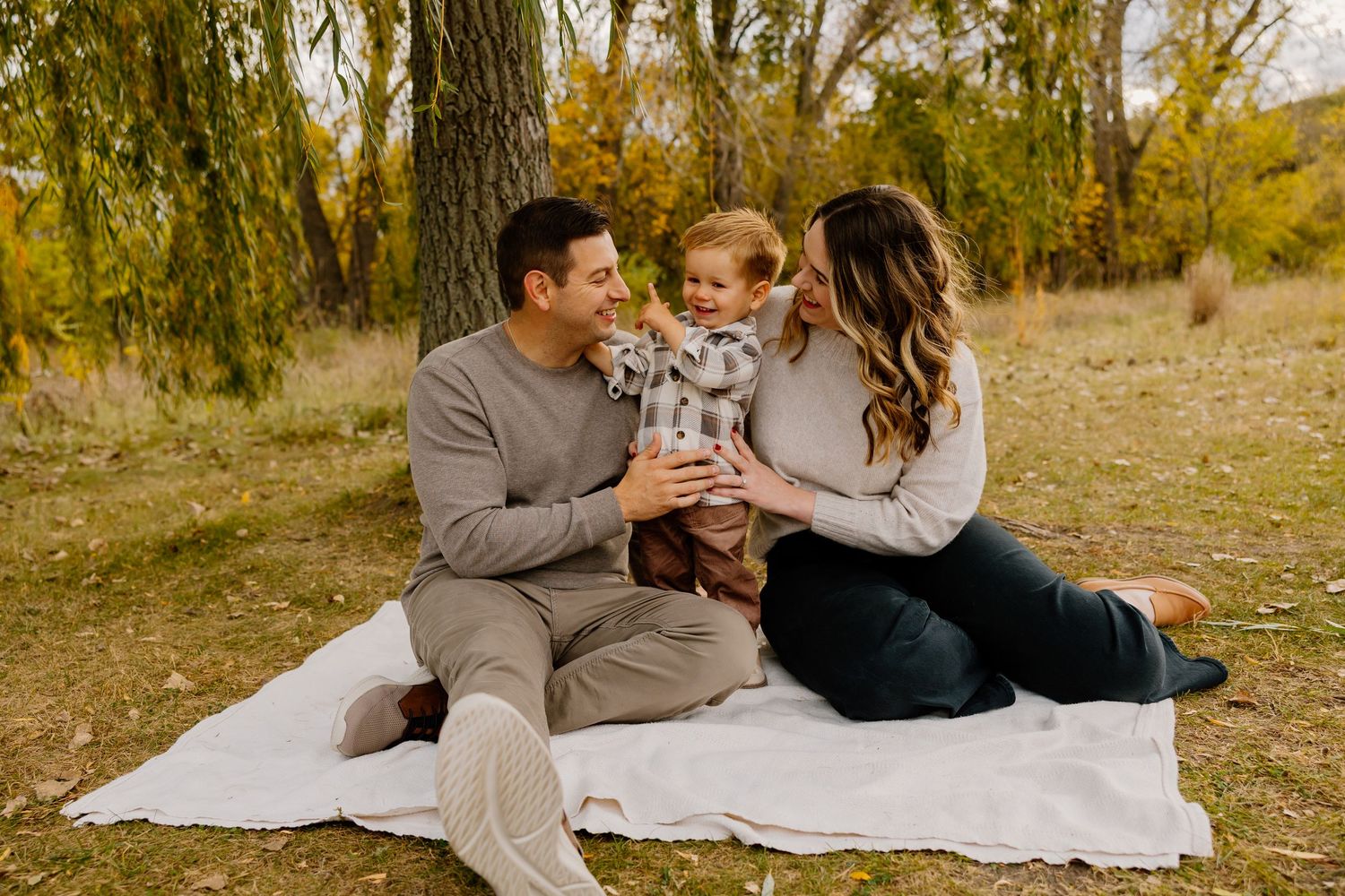 A romantic autumn photoshoot on a picnic blanket surrounded by golden fall foliage in a wooded setting.