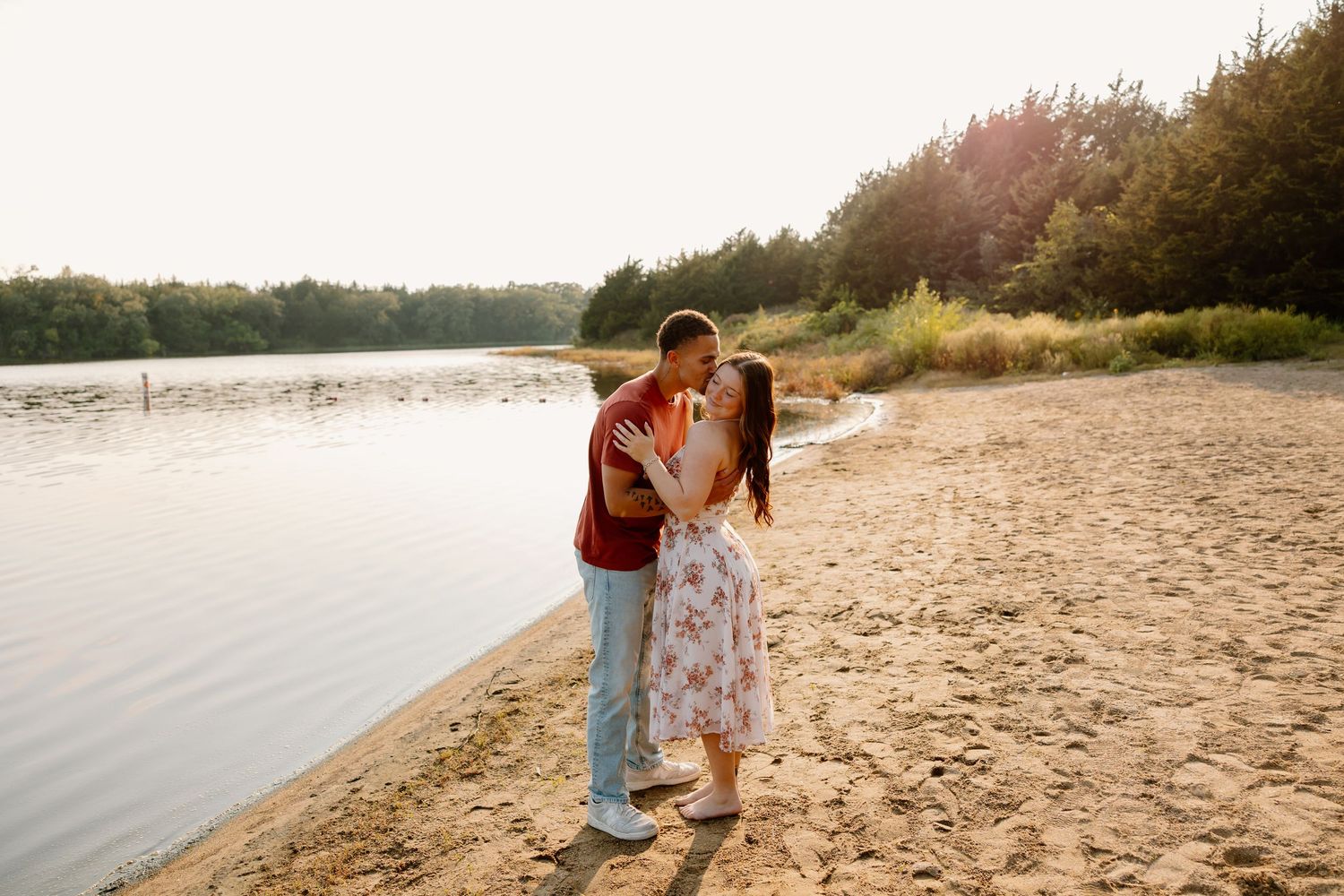 A couple stands together on a sandy beach during golden hour at sunset.