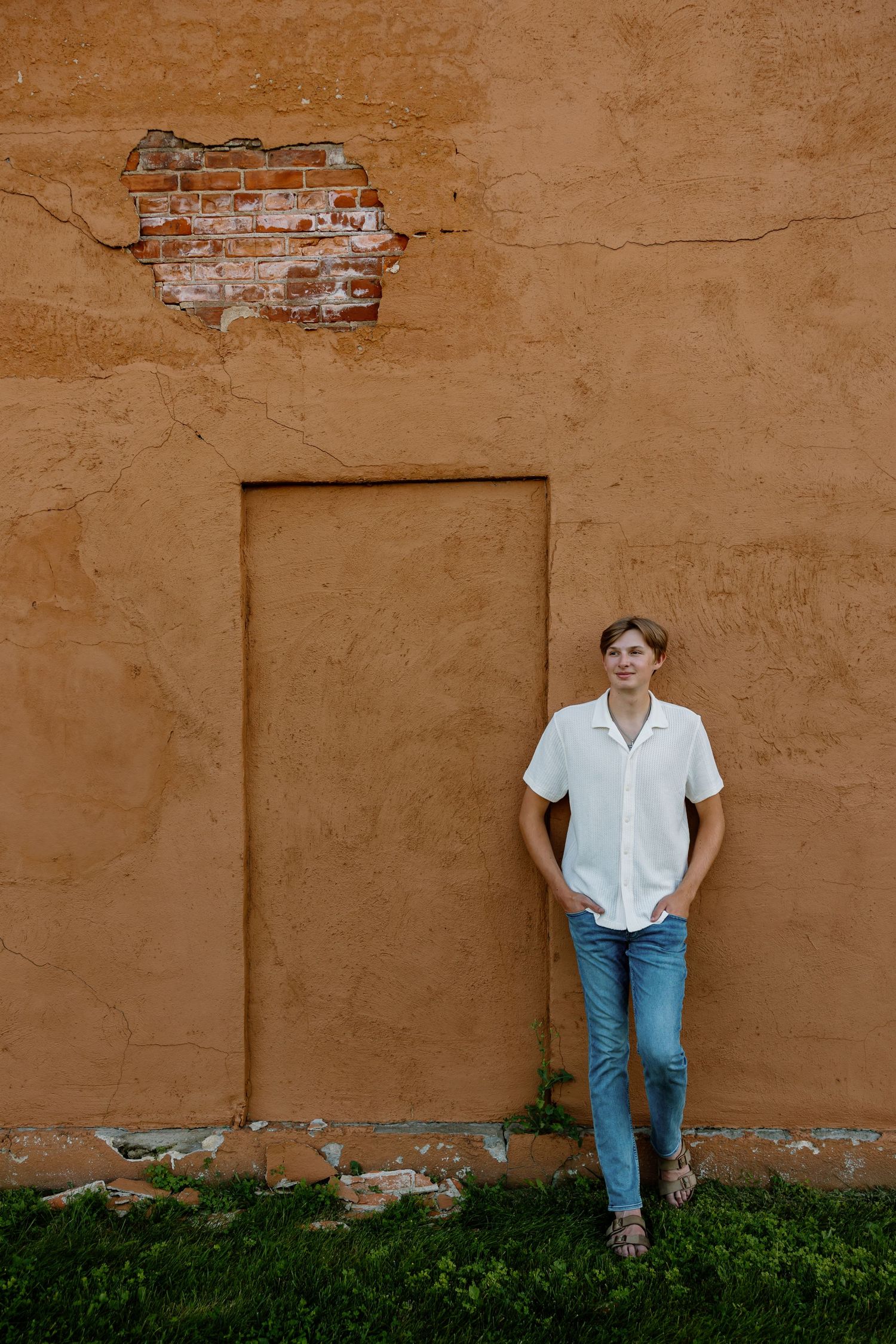 Person in white shirt and jeans poses against textured terracotta wall.