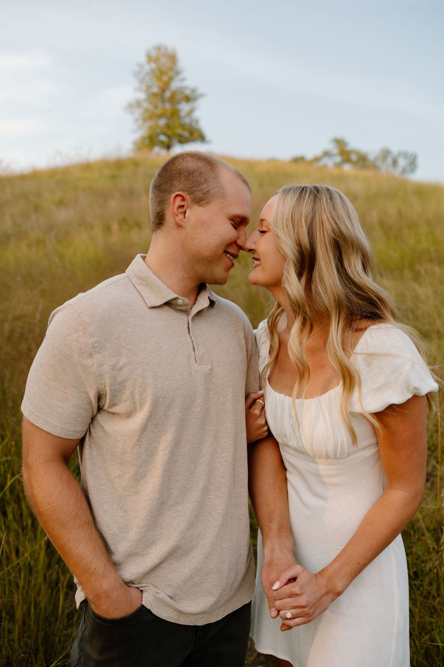 A couple embraces in a sunlit field wearing coordinated beige and white outfits.