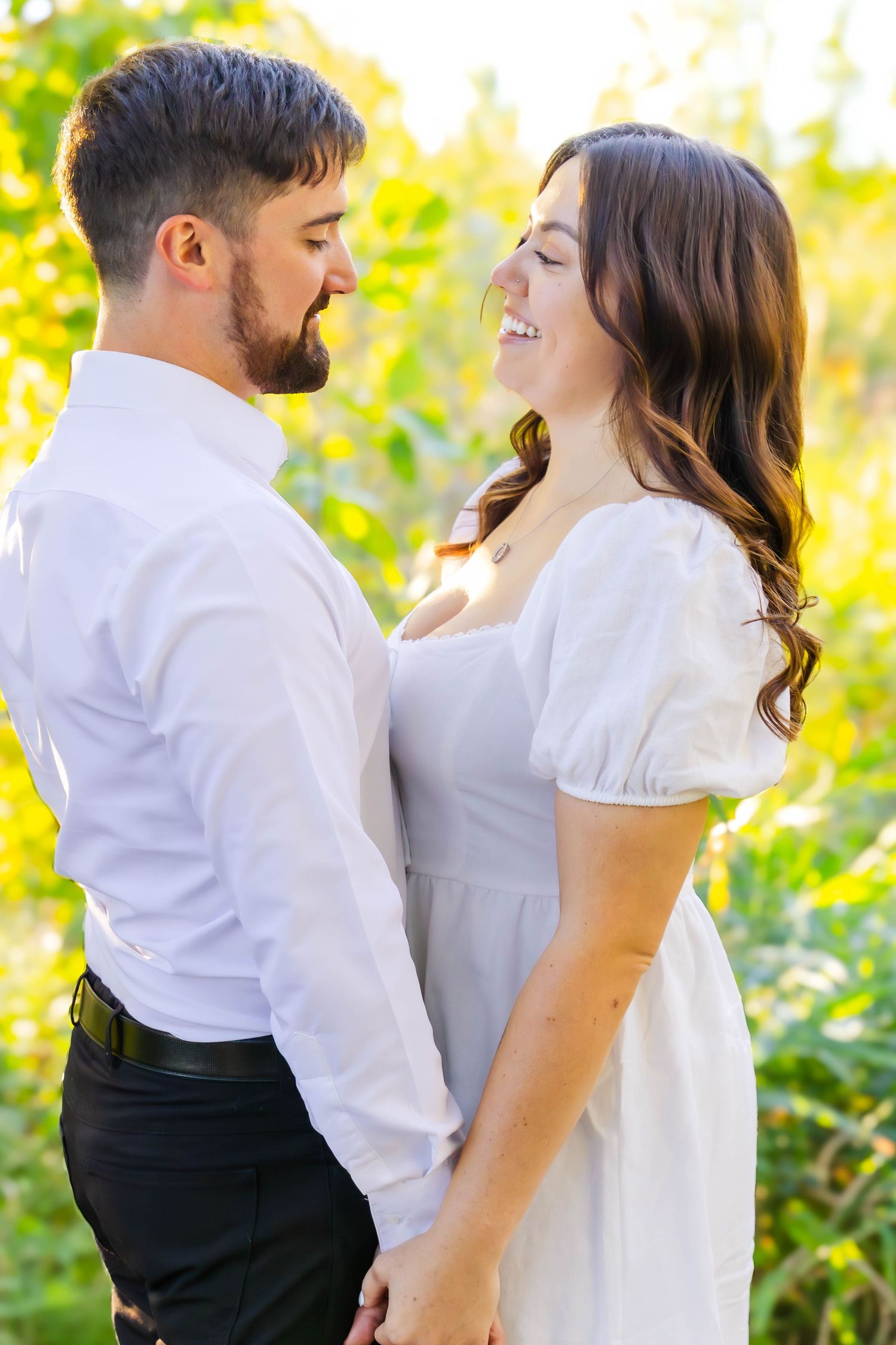 Romantic couple shares tender moments in white attire against lush green natural backdrop.
