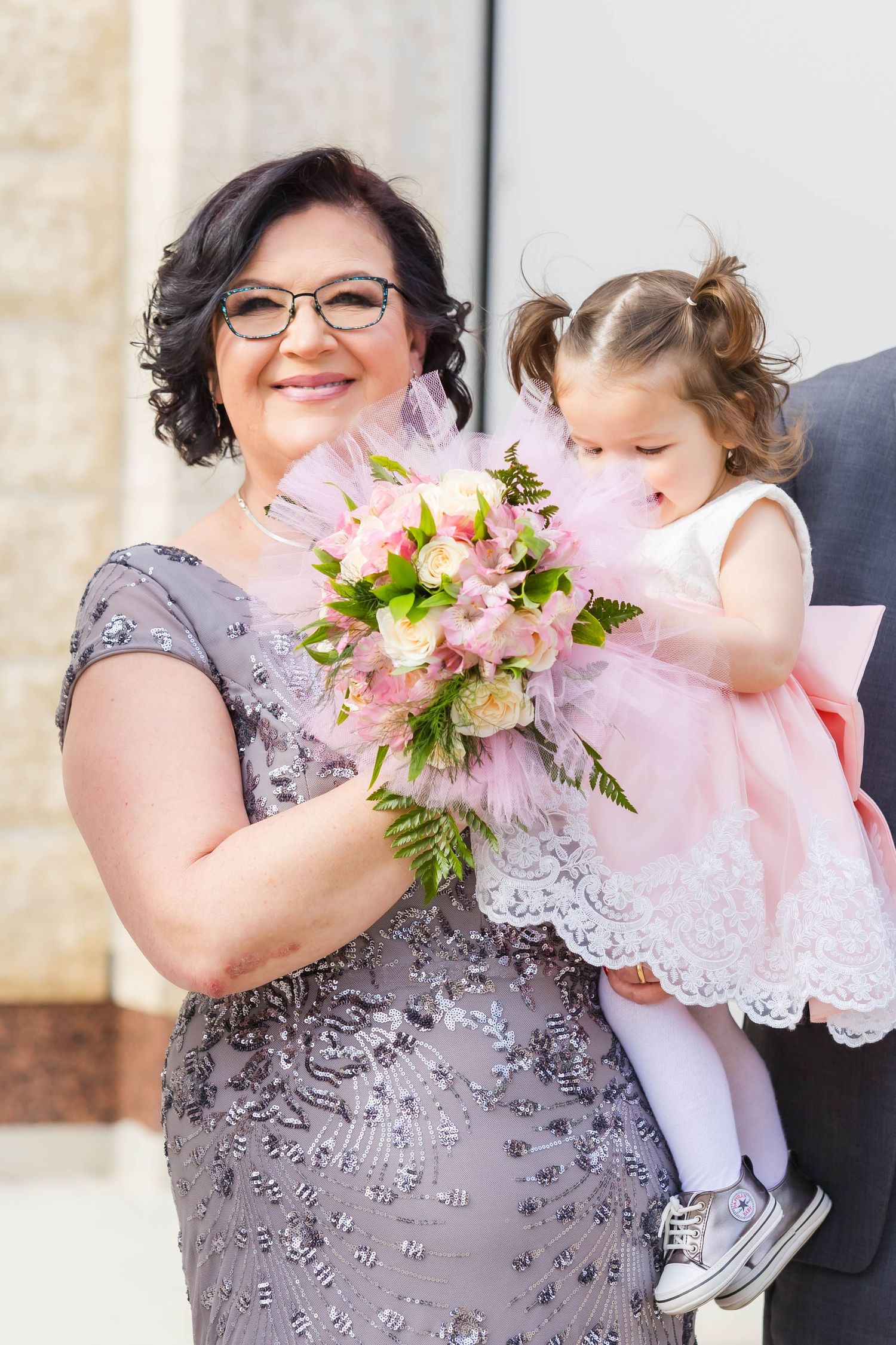 Wedding party member in gray lace dress holds young attendant in pink dress with floral details.