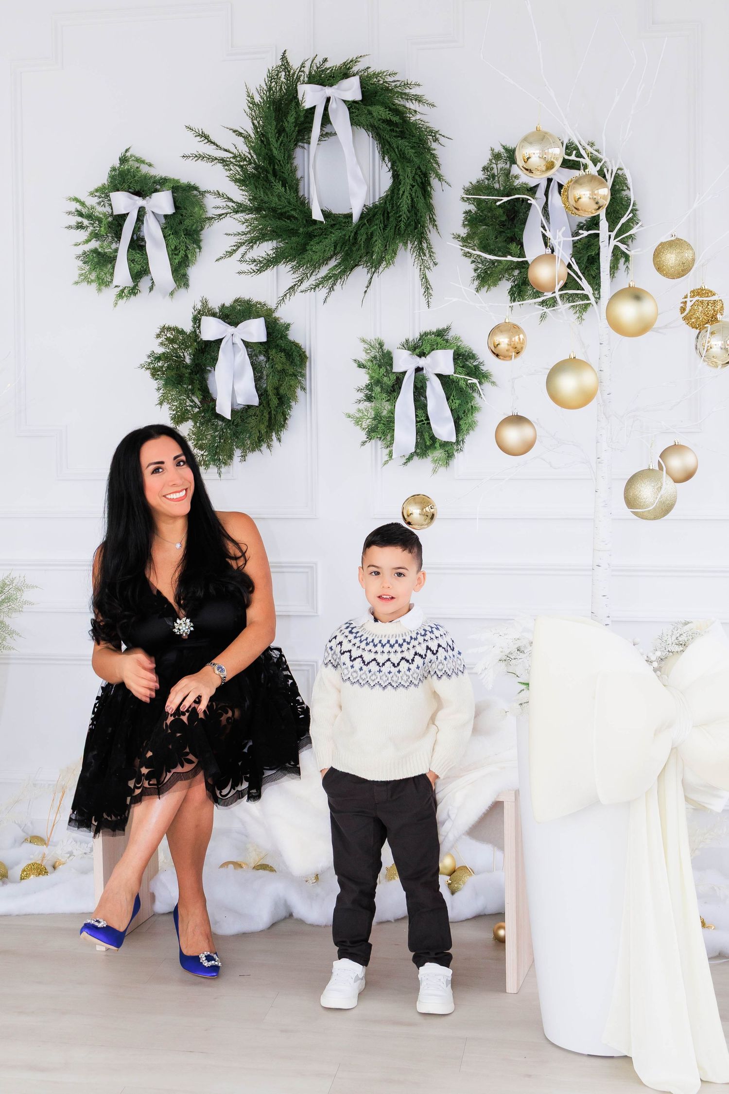 Holiday photo shoot with festive evergreen wreaths and gold ornaments against white backdrop.