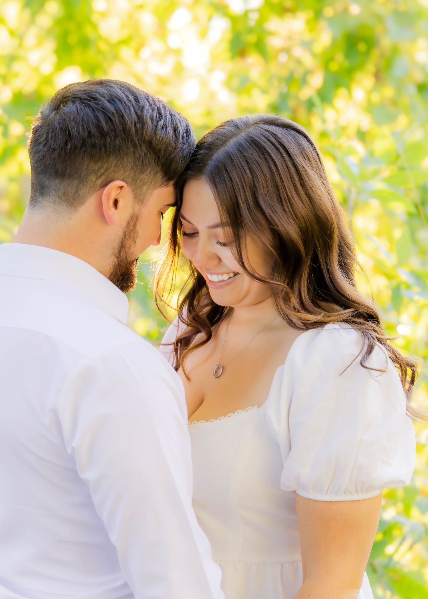 Romantic couple in white clothing sharing intimate moments outdoors with green foliage in background.