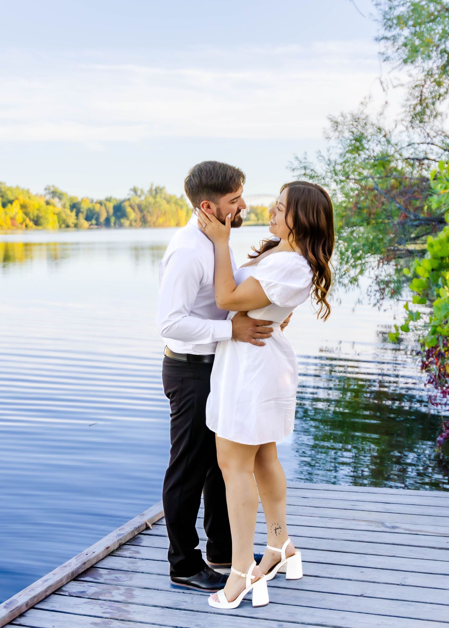 A romantic couple shares an intimate moment on a wooden dock by a serene lake during a summer afternoon.