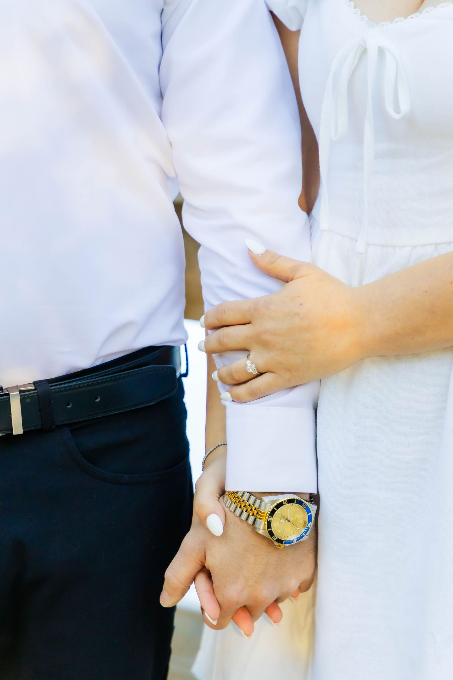 Close-up shot of a couple's hands and torso showing white clothing and accessories.