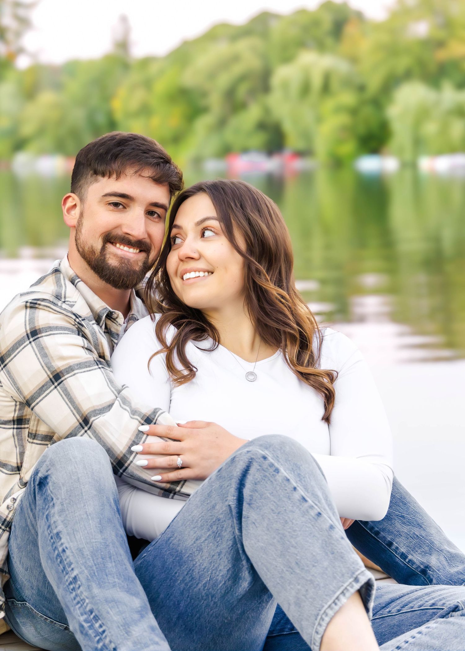 Happy couple in casual wear cuddle on wooden dock by tranquil lake.