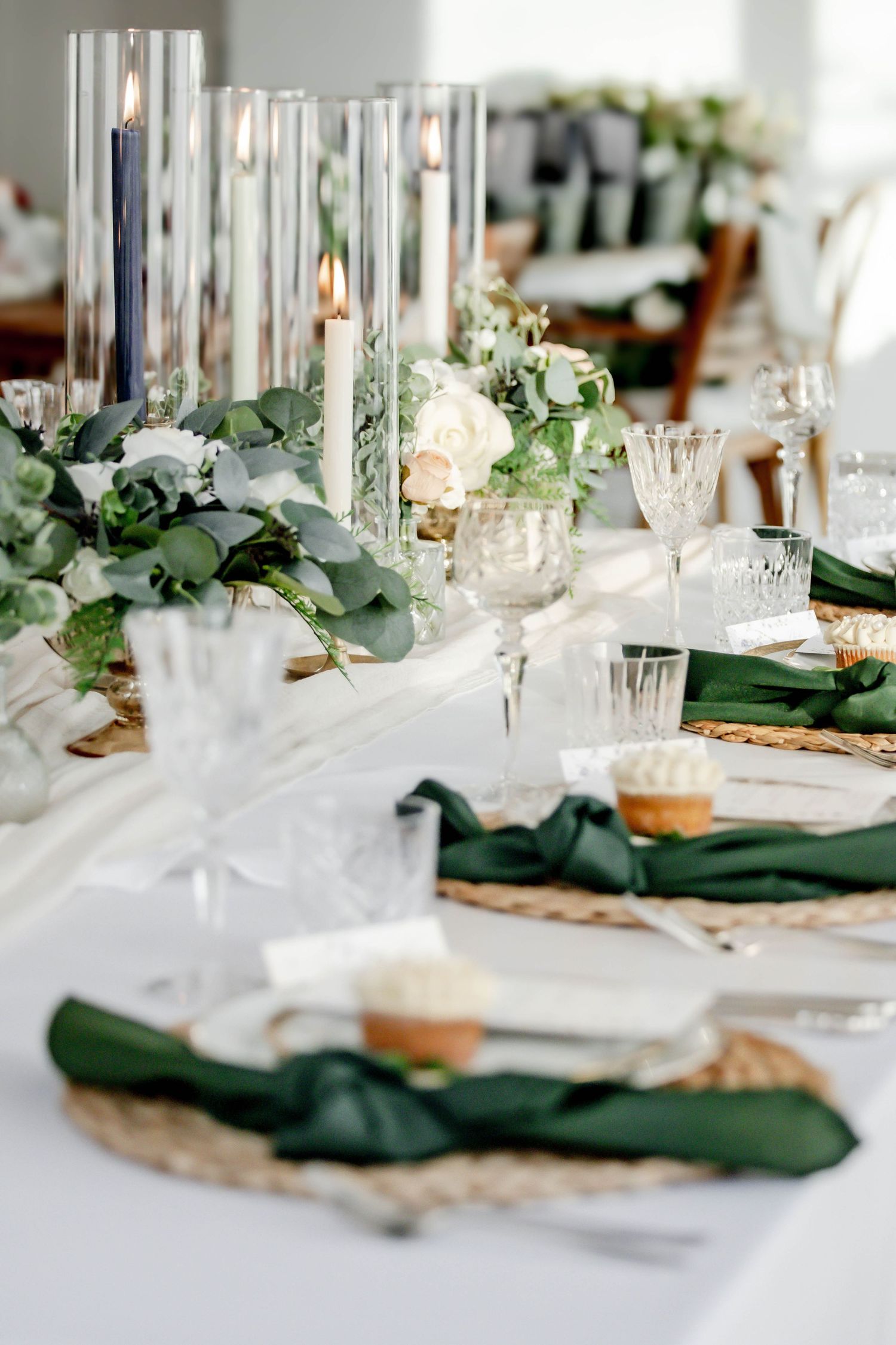 Modern wedding reception table with dark green napkins and crystal glasses in natural light.