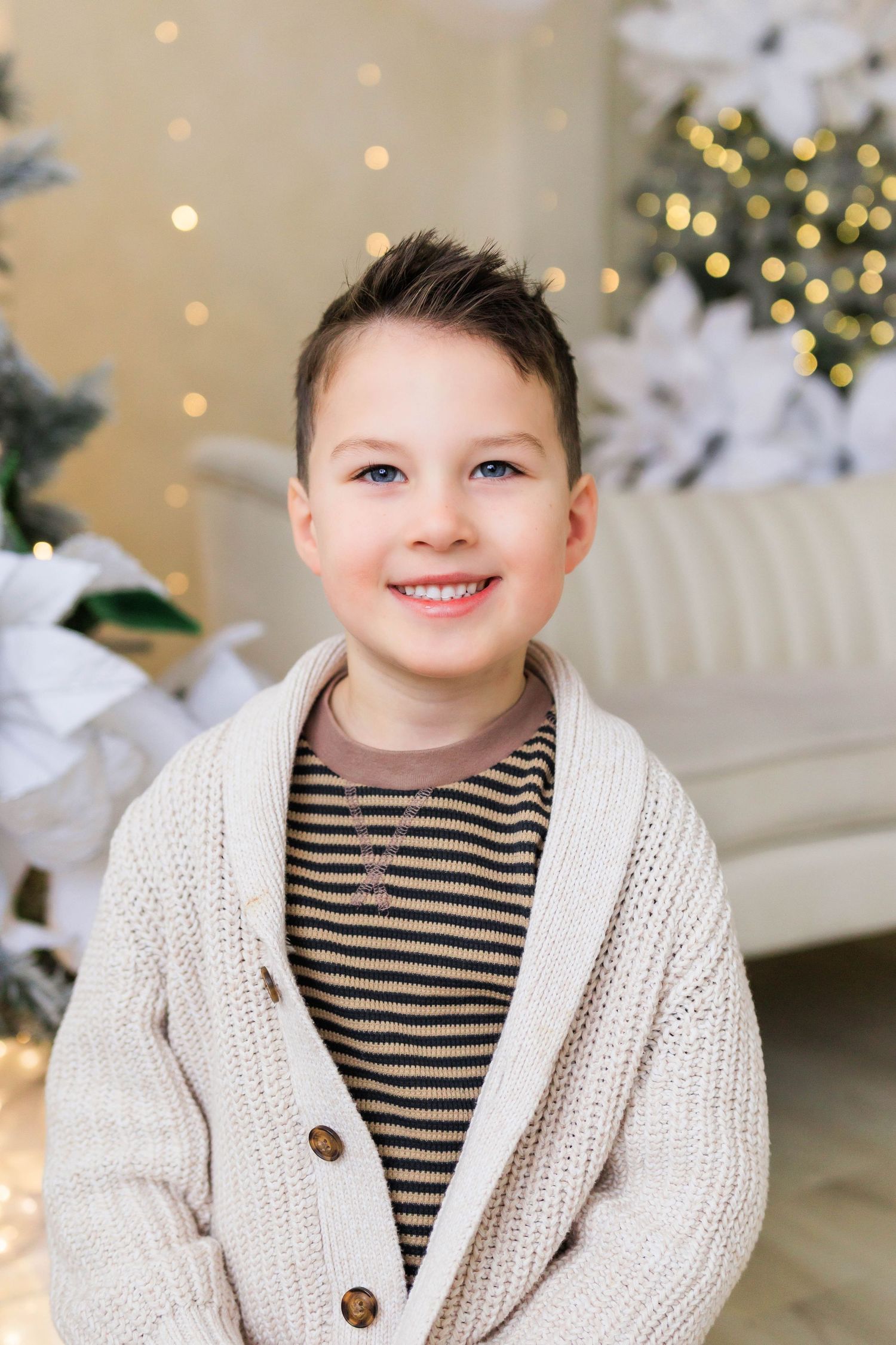 Winter portrait with cozy white cardigan and striped shirt against festive backdrop.