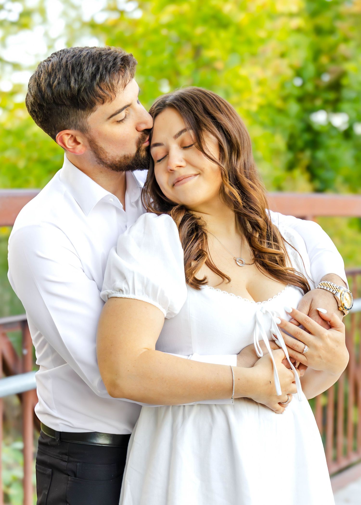 A romantic couple in white embraces and shares tender moments on an outdoor wooden deck surrounded by greenery.