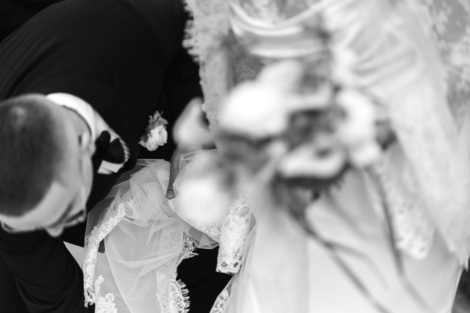 Black and white wedding photo of bride and groom exchanging vows, bride in lace gown holding bouquet.
