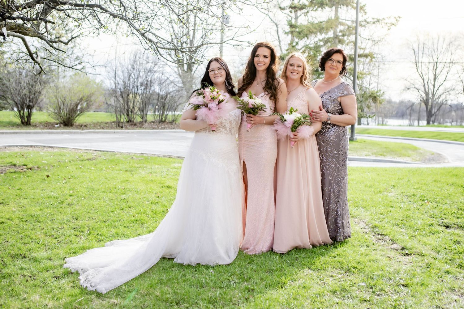 Spring wedding party in pink and white dresses poses on grassy lawn under blooming trees.