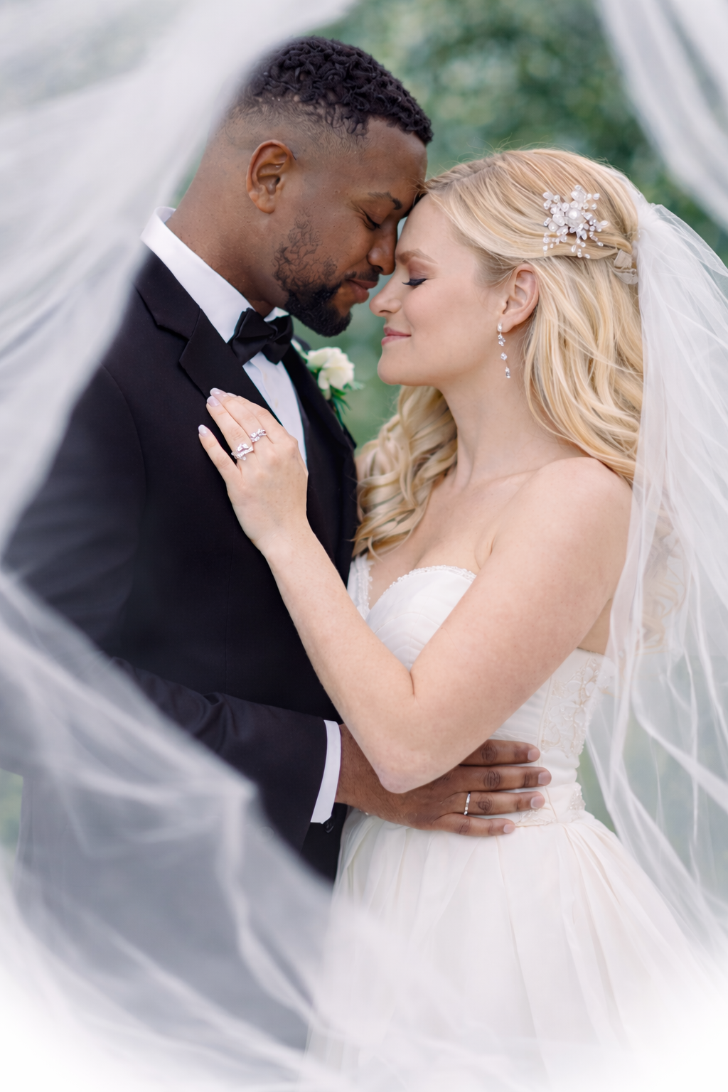 Romantic wedding portrait of newlyweds sharing an intimate moment under flowing white veil outdoors.