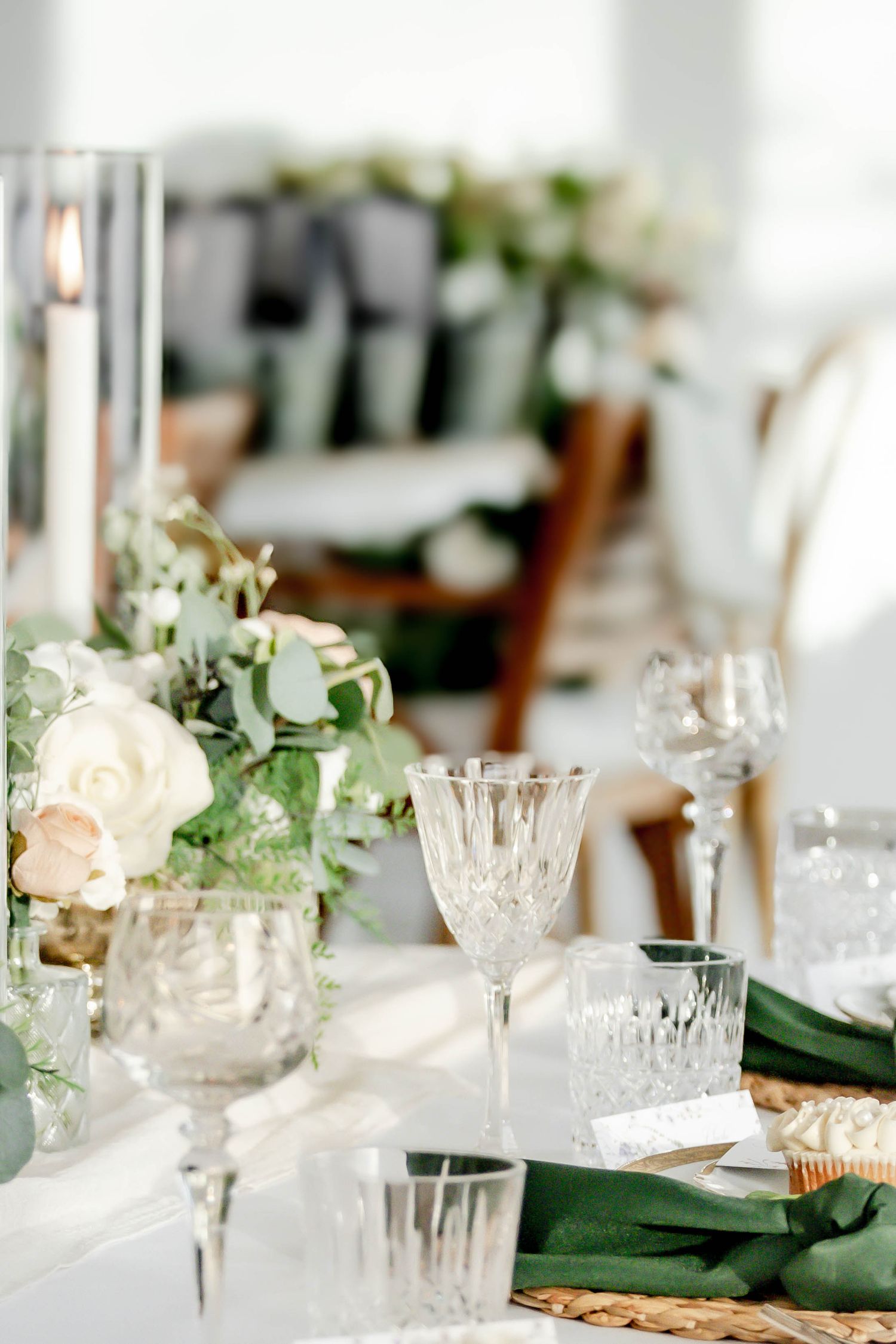 Elegant table setting with crystal glassware, white candles and soft floral arrangements on a white tablecloth.