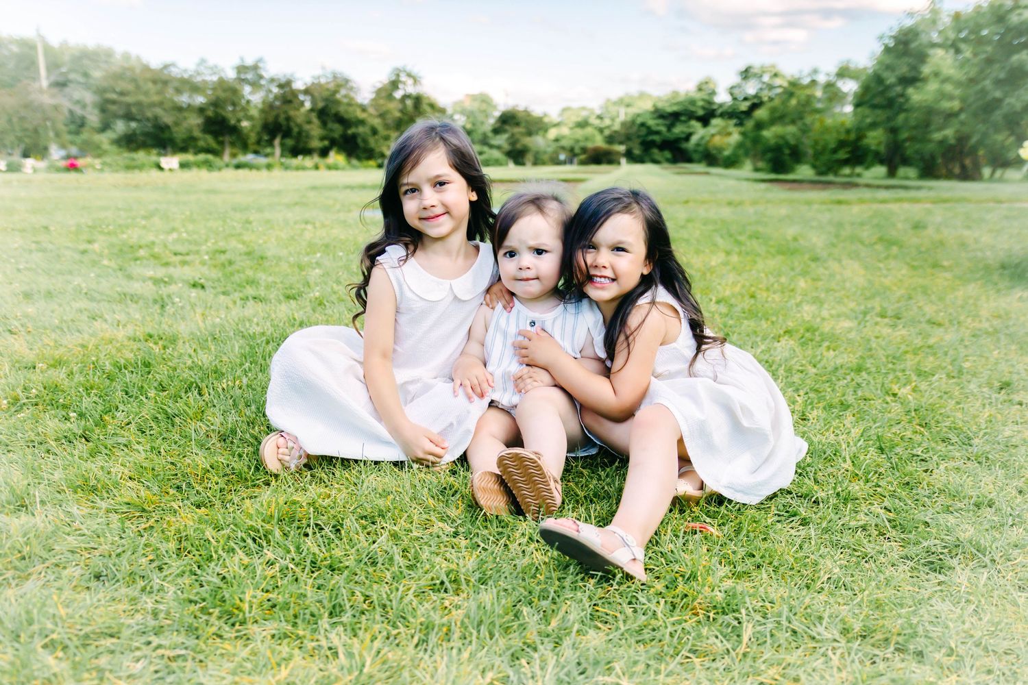 Family members laying on grass in matching white outfits during outdoor photo session.