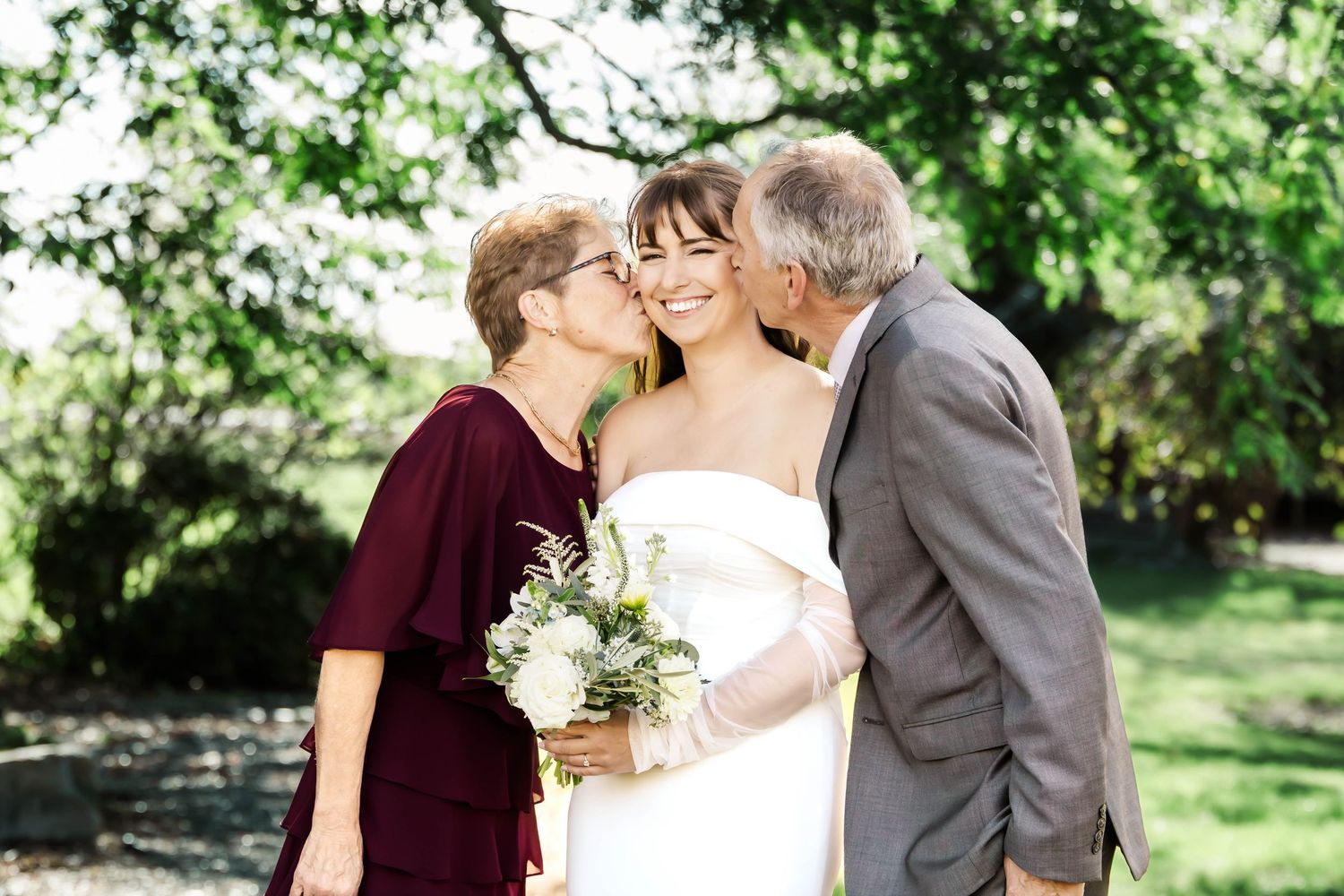 A couple shares a romantic kiss in a lush garden setting during their wedding celebration.