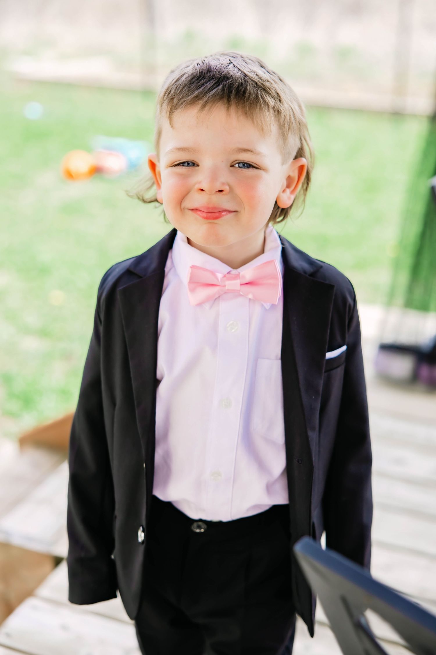 Young ring bearer in black suit and pink bow tie smiling at camera.
